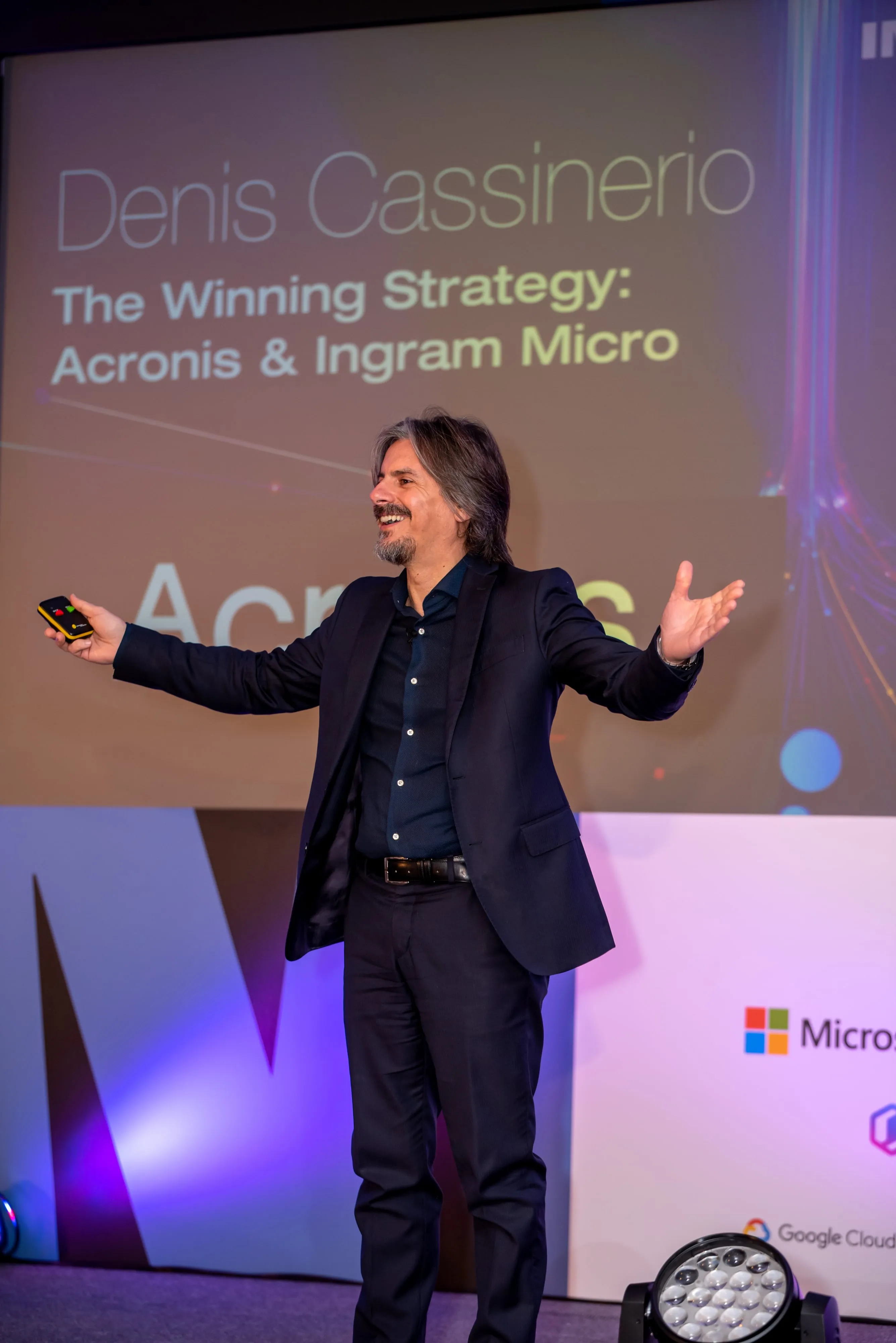 Keynote speaker on stage gesturing to crowd at corporate tech conference