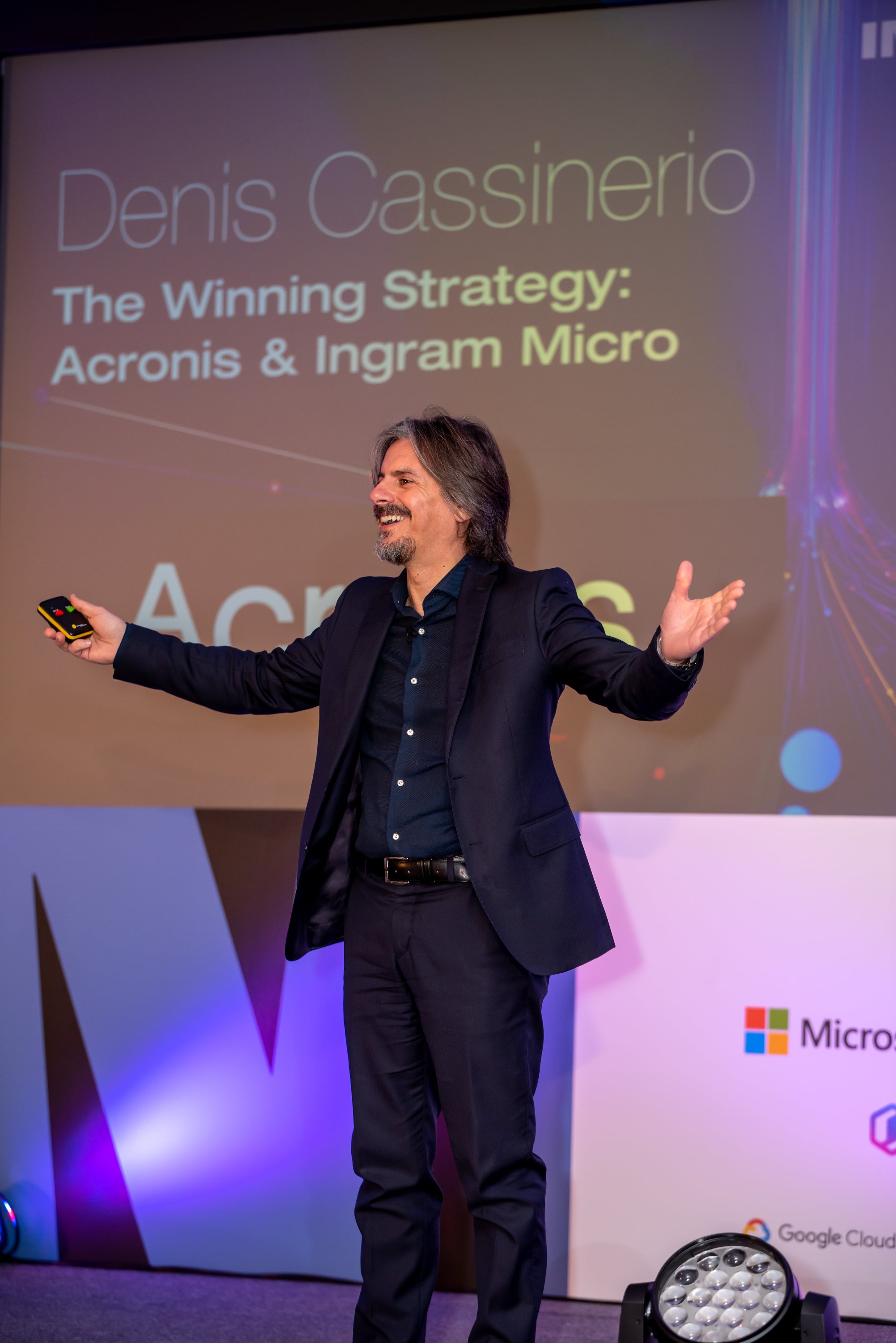 Keynote speaker on stage gesturing to crowd at corporate tech conference