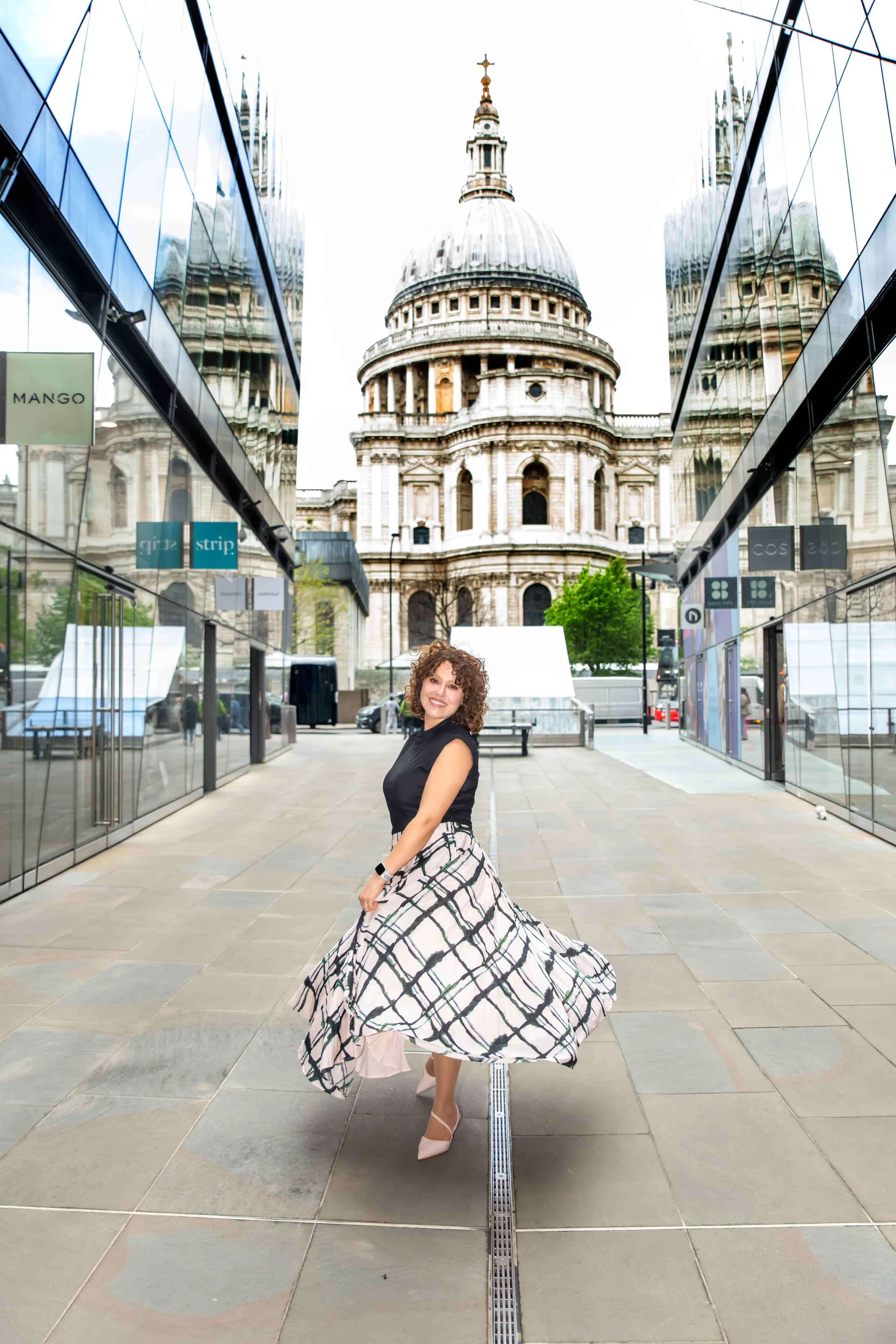 Personal-brand portrait at St Paul's Cathedral — woman twirling plaid maxi skirt in glass-walled approach corridor