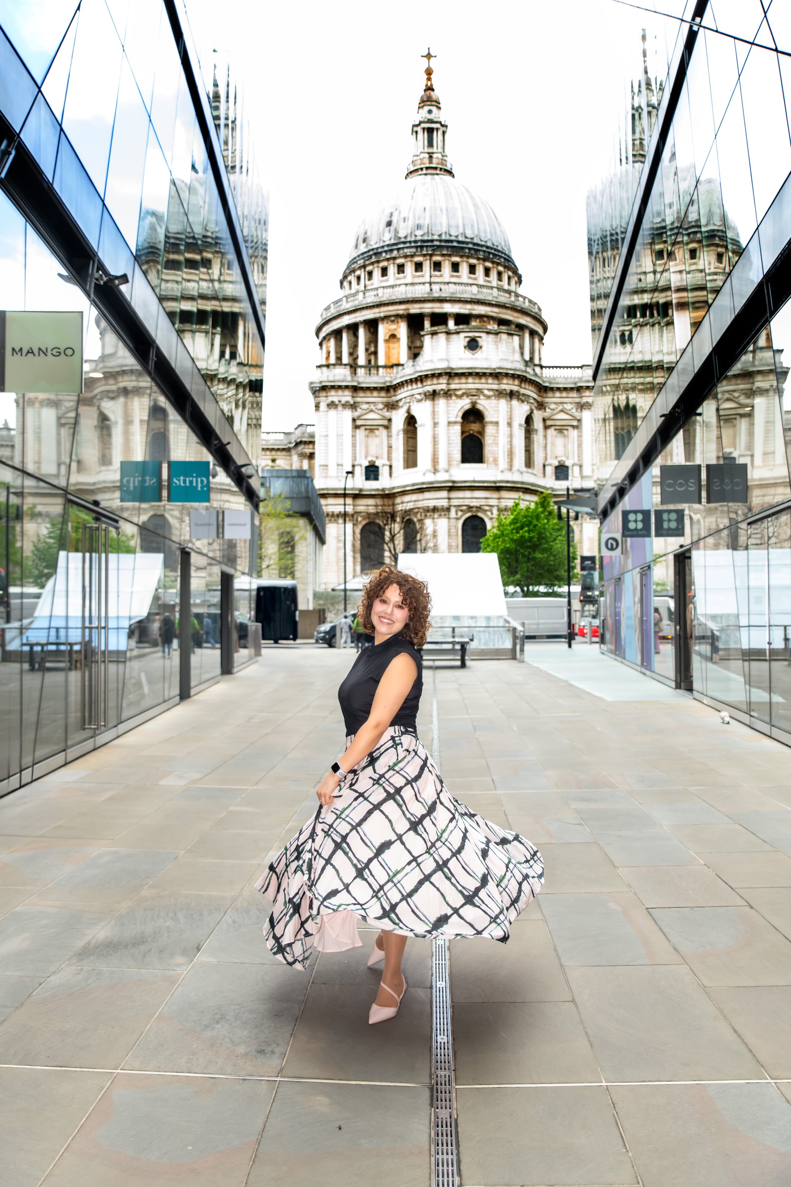 Personal-brand portrait at St Paul's Cathedral — woman twirling plaid maxi skirt in glass-walled approach corridor
