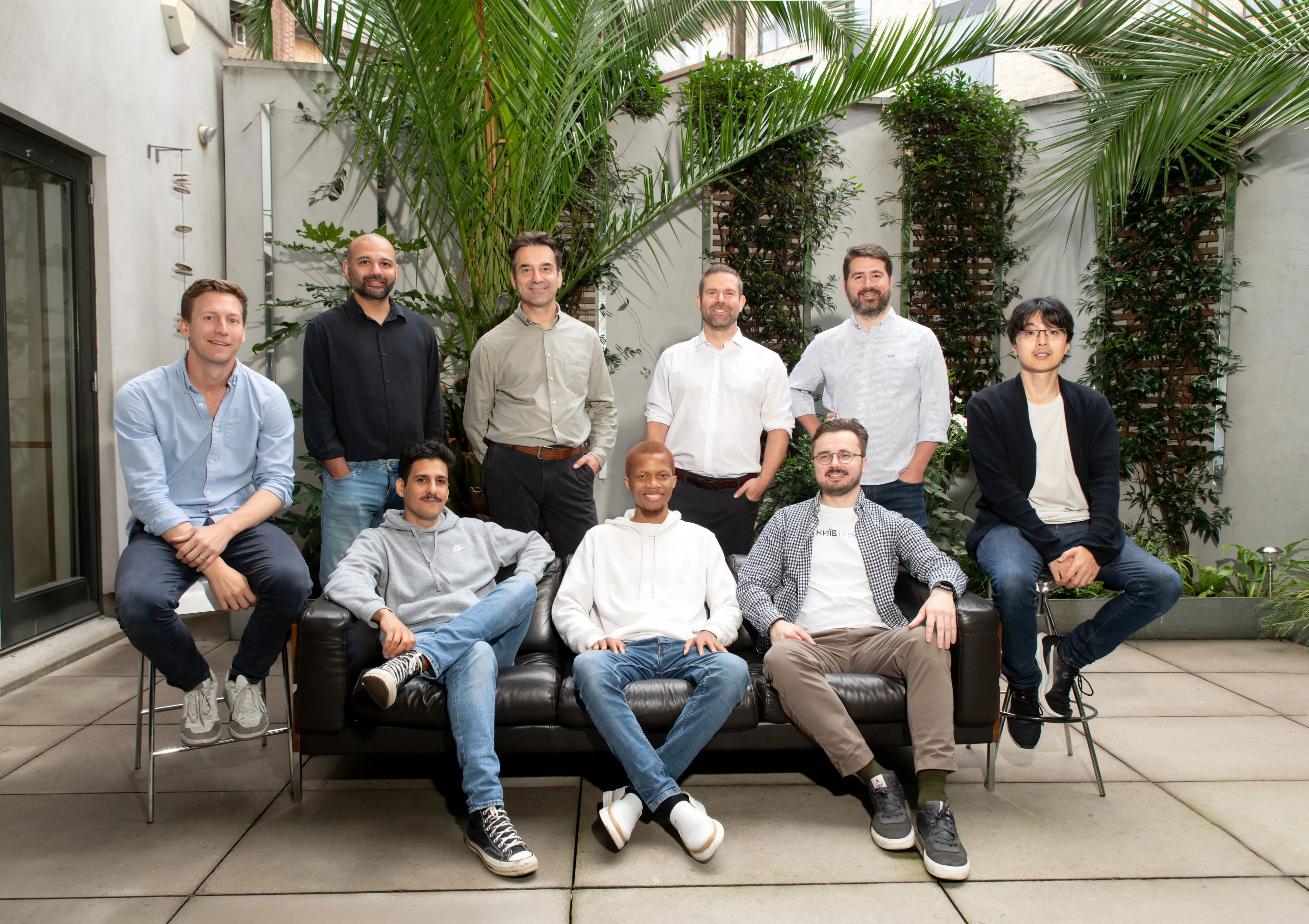 Sprout AI team member solo portrait on a stool in the courtyard, navy blazer over white shirt, palms behind