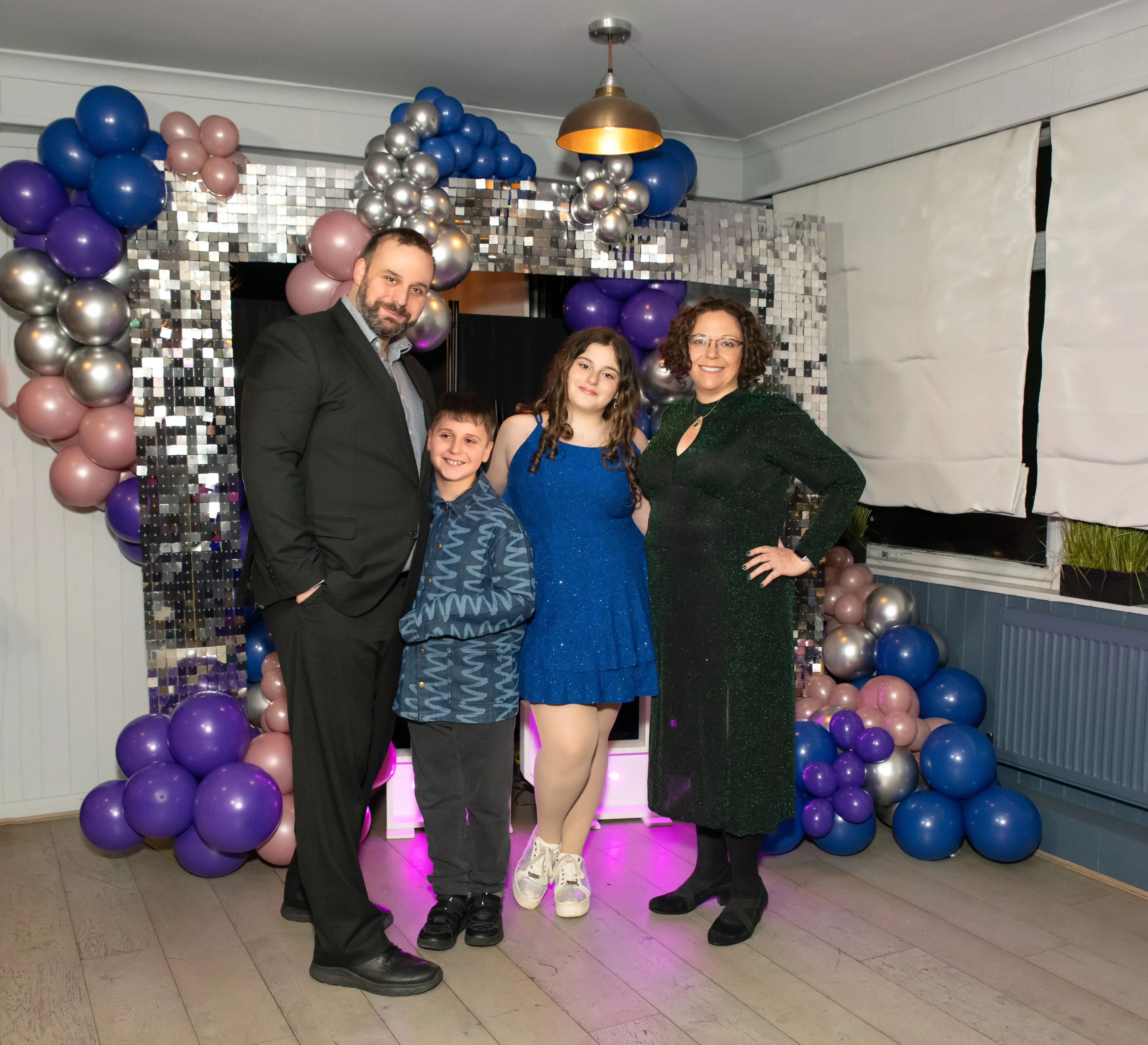 Family of four pose in front of a silver-sequin and balloon disco arch at the bat mitzvah party