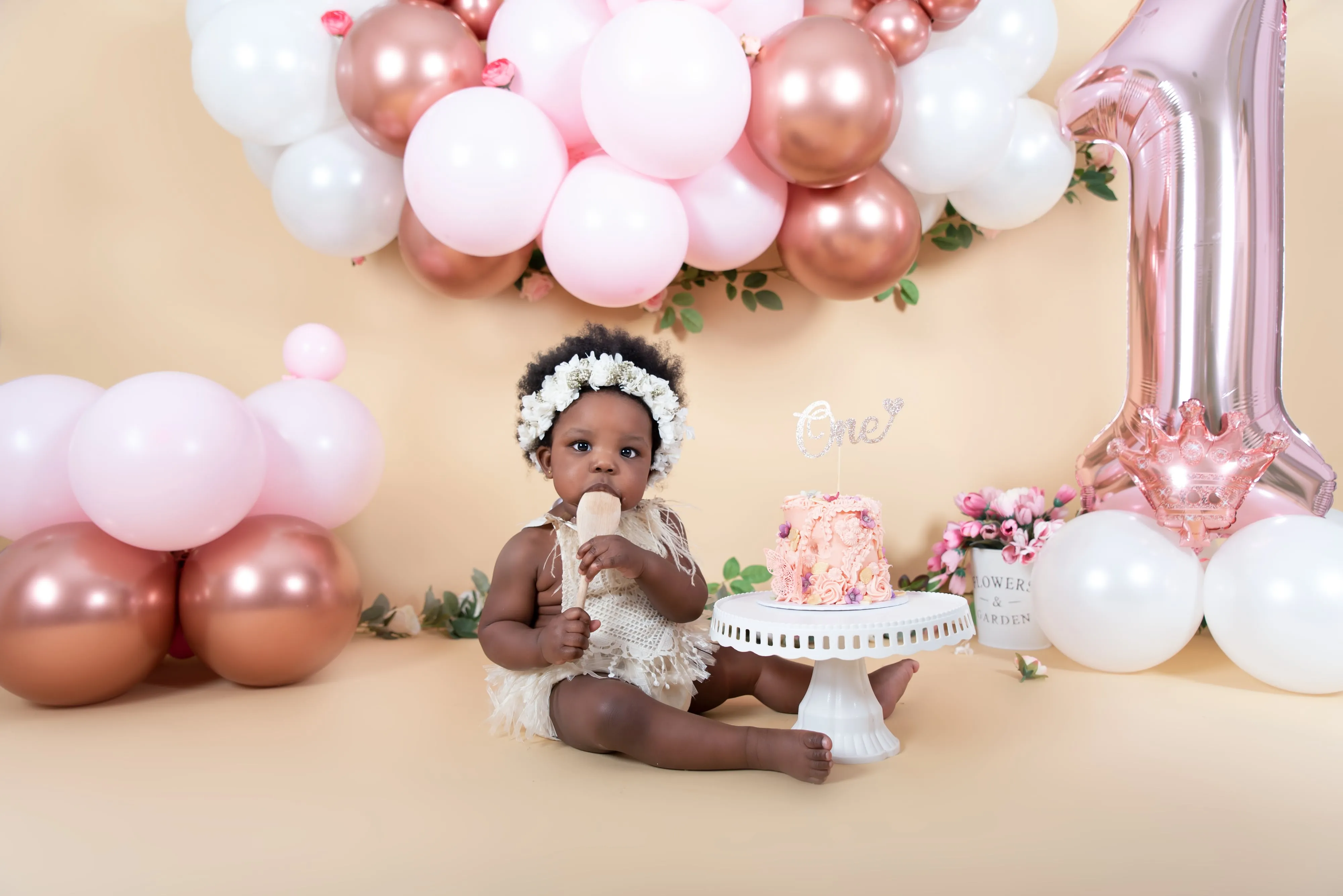 Baby girl with floral crown by cake at first birthday session