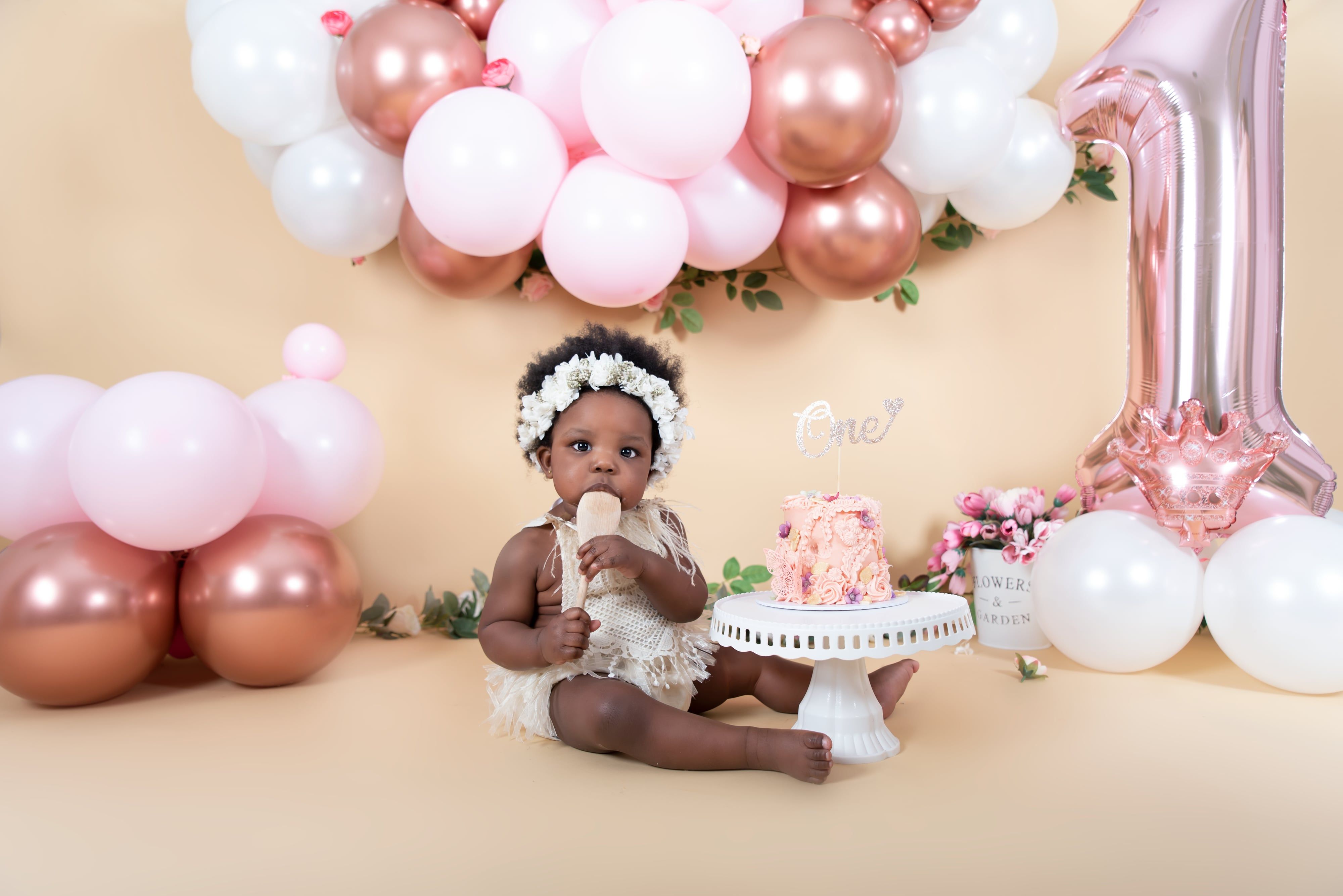 Baby girl with floral crown by cake at first birthday session