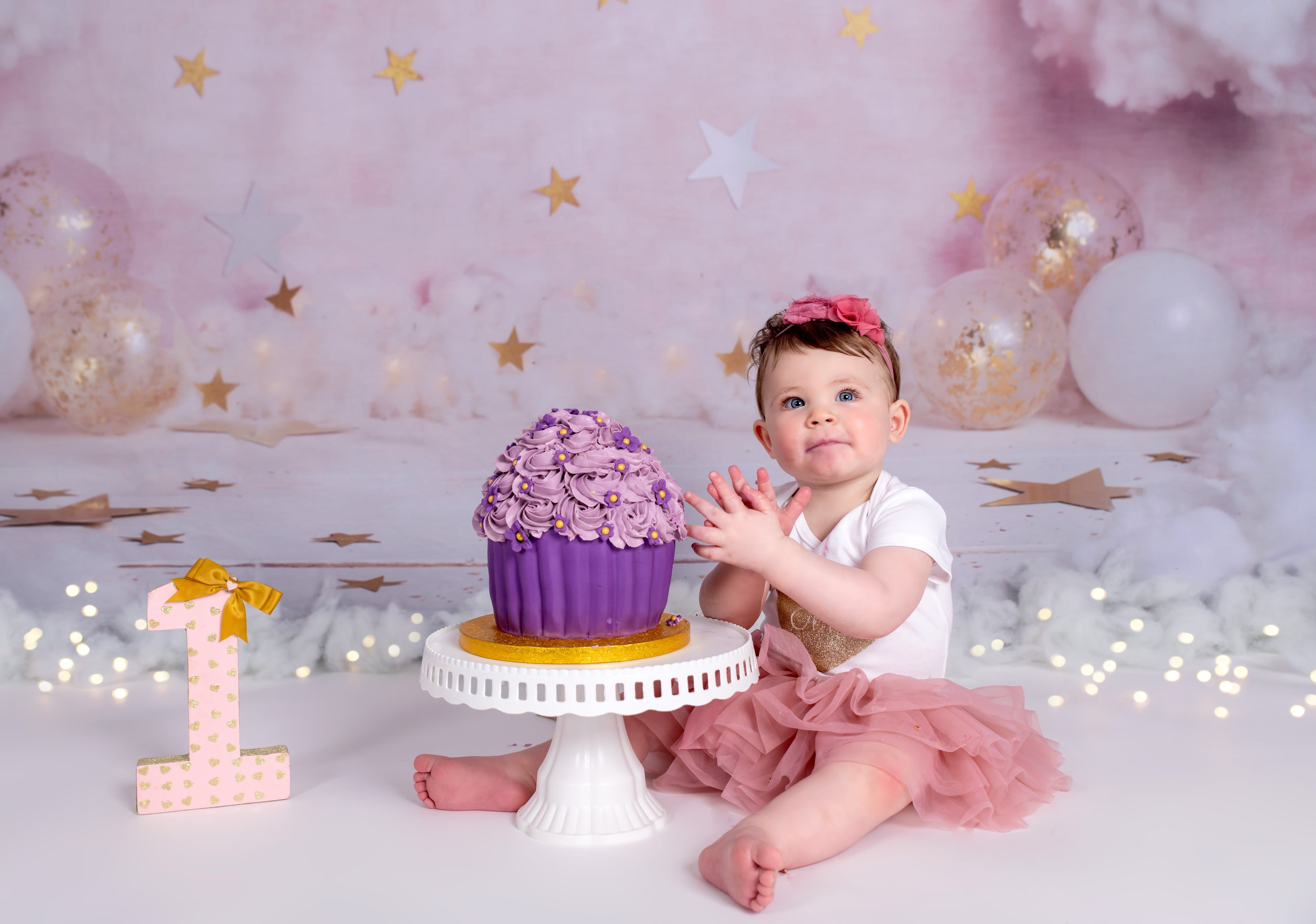 Toddler in pink tutu touches purple giant cupcake with gold 1 on pink stars-and-clouds set
