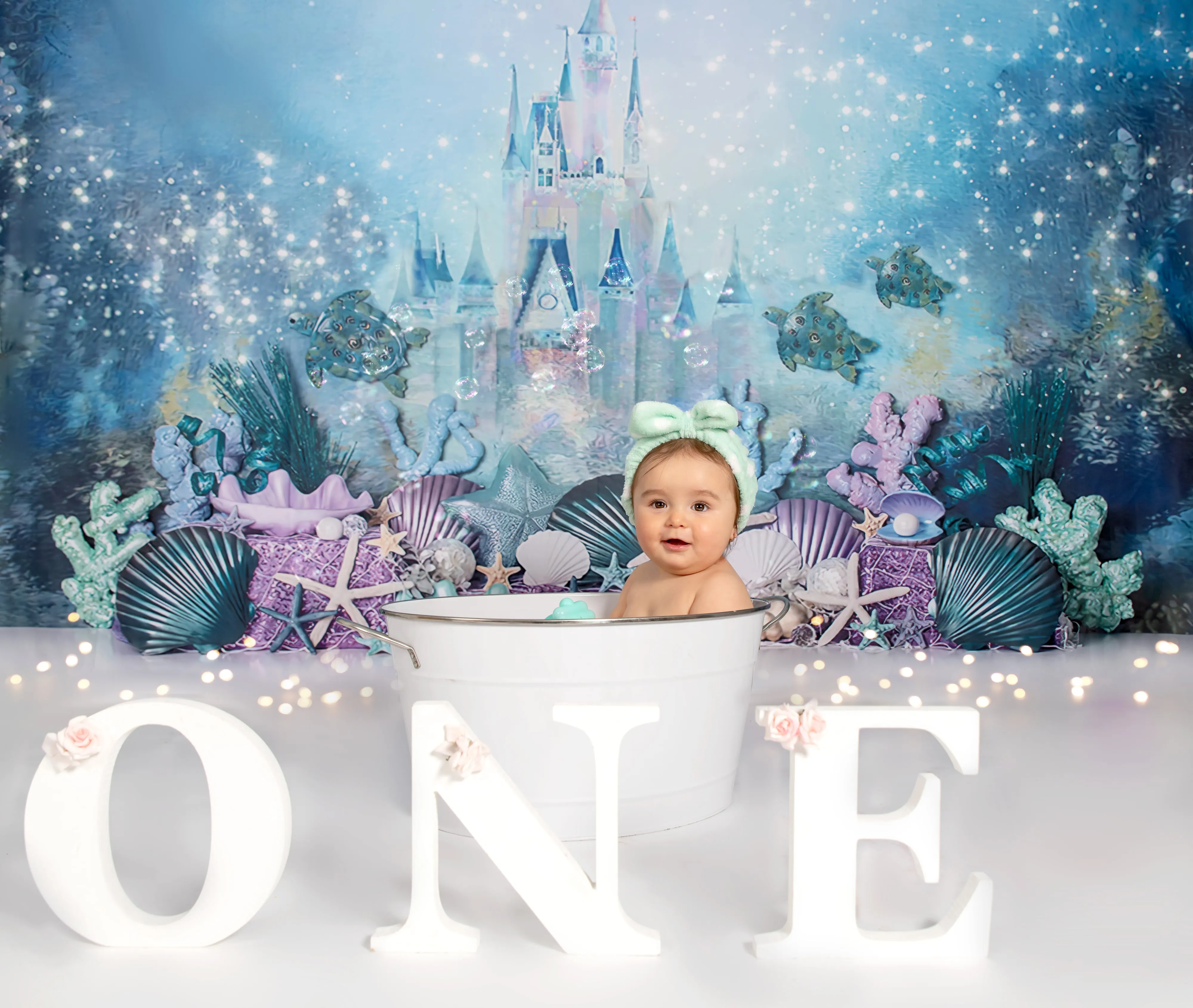 Baby in mint headband sits in tin tub on Disney castle under-the-sea aqua and purple backdrop