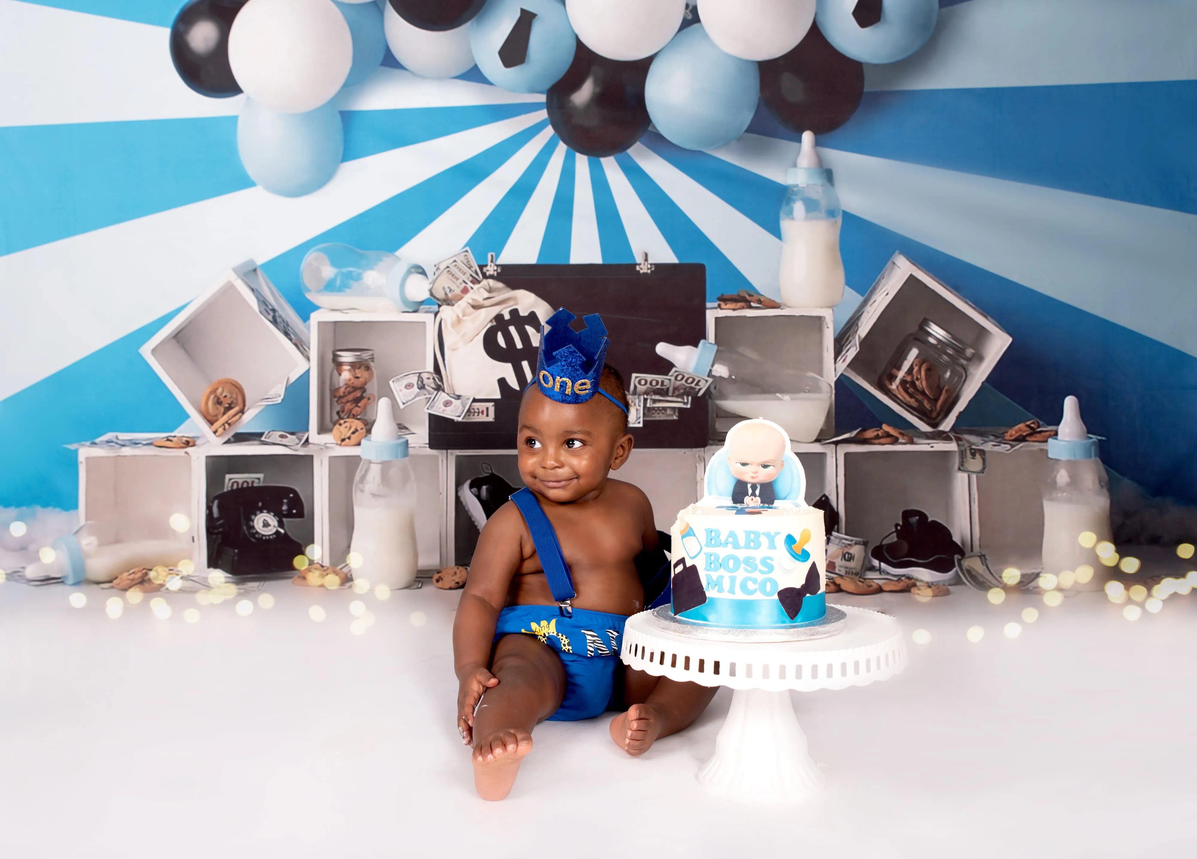 Toddler boy in blue suspenders with Baby Boss cake on blue-and-white striped balloon set