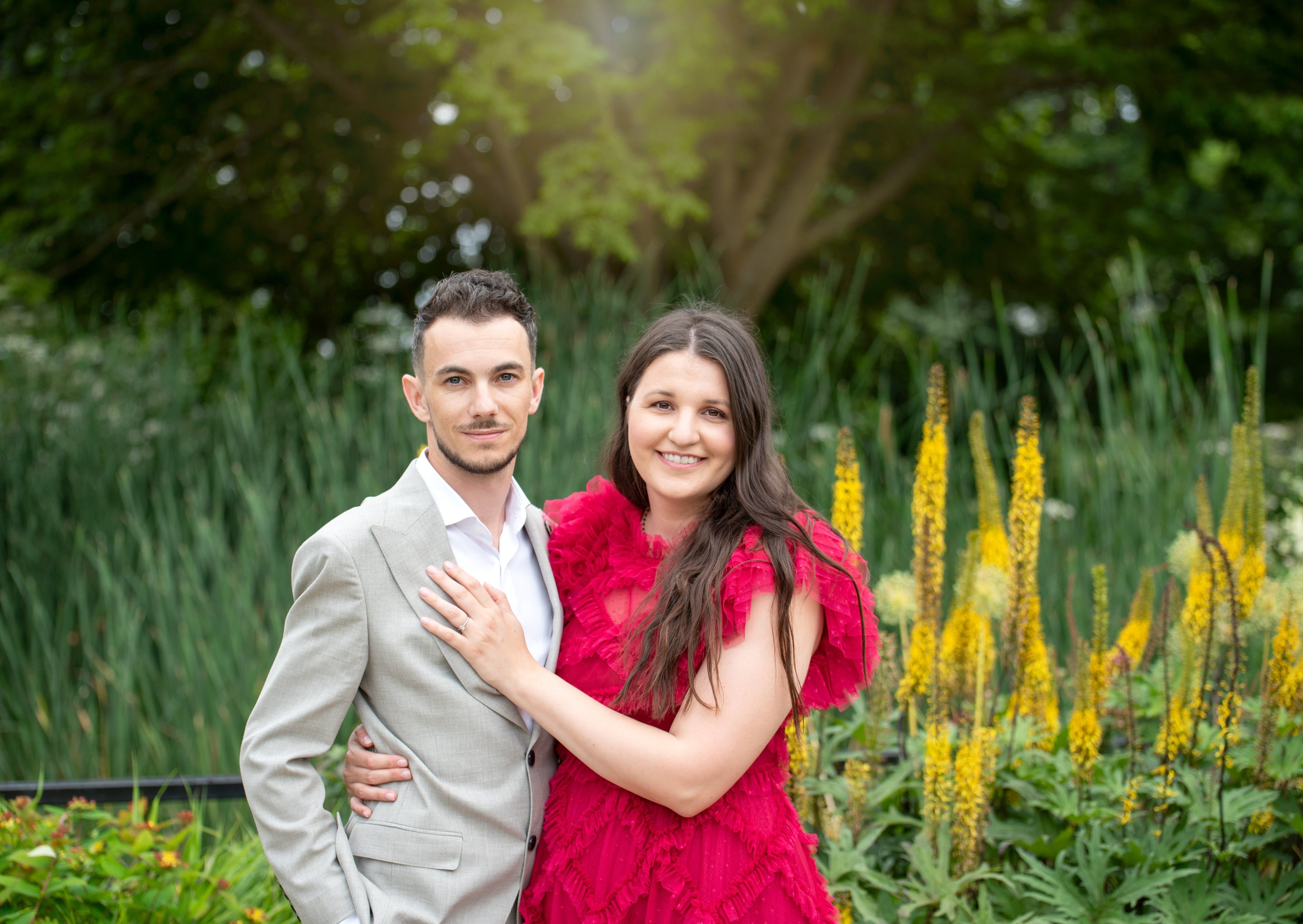 Couple dressed for a christening embrace among golden garden blooms on a summer afternoon