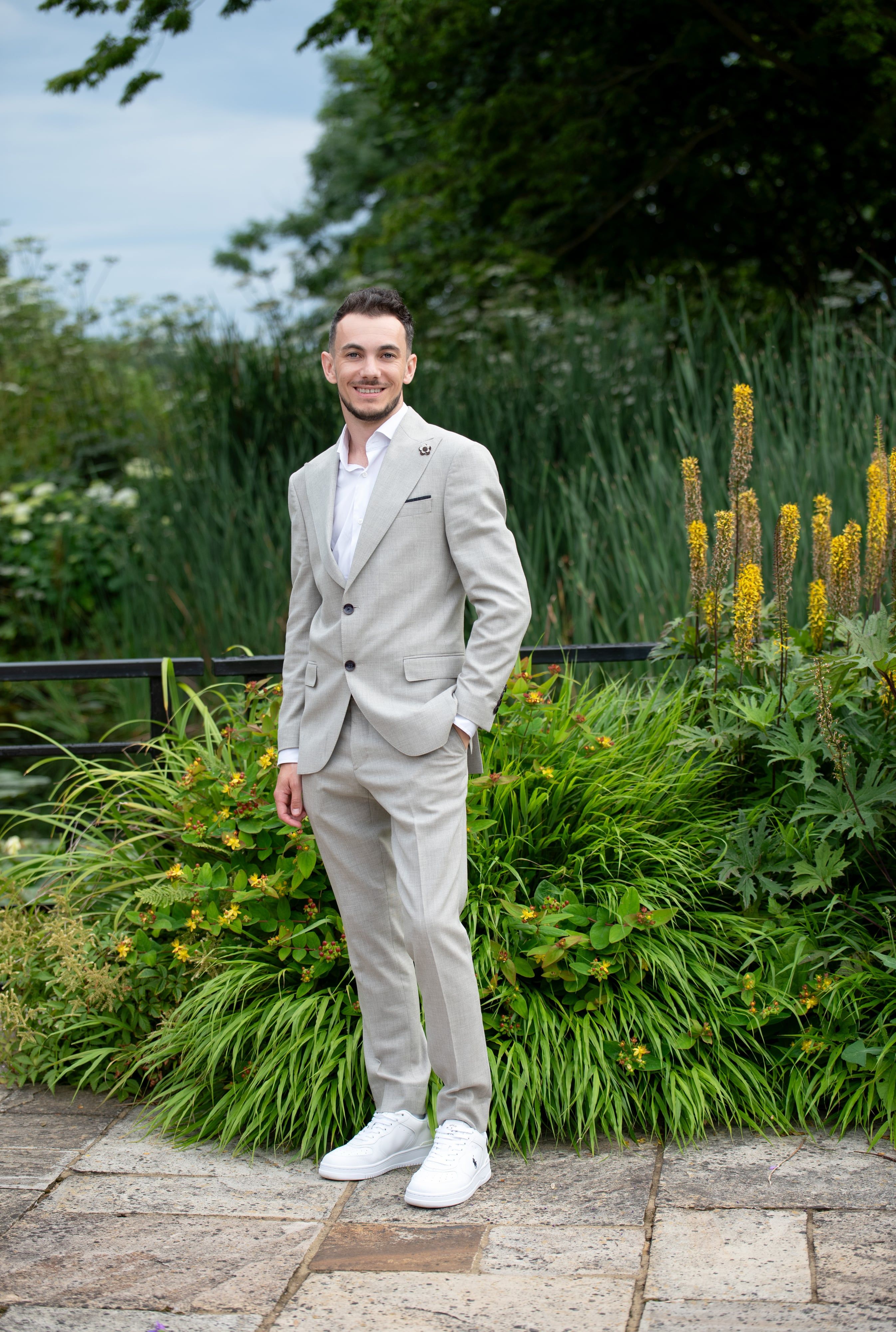 Father in a pale linen suit stands relaxed before lush green borders in a summer garden