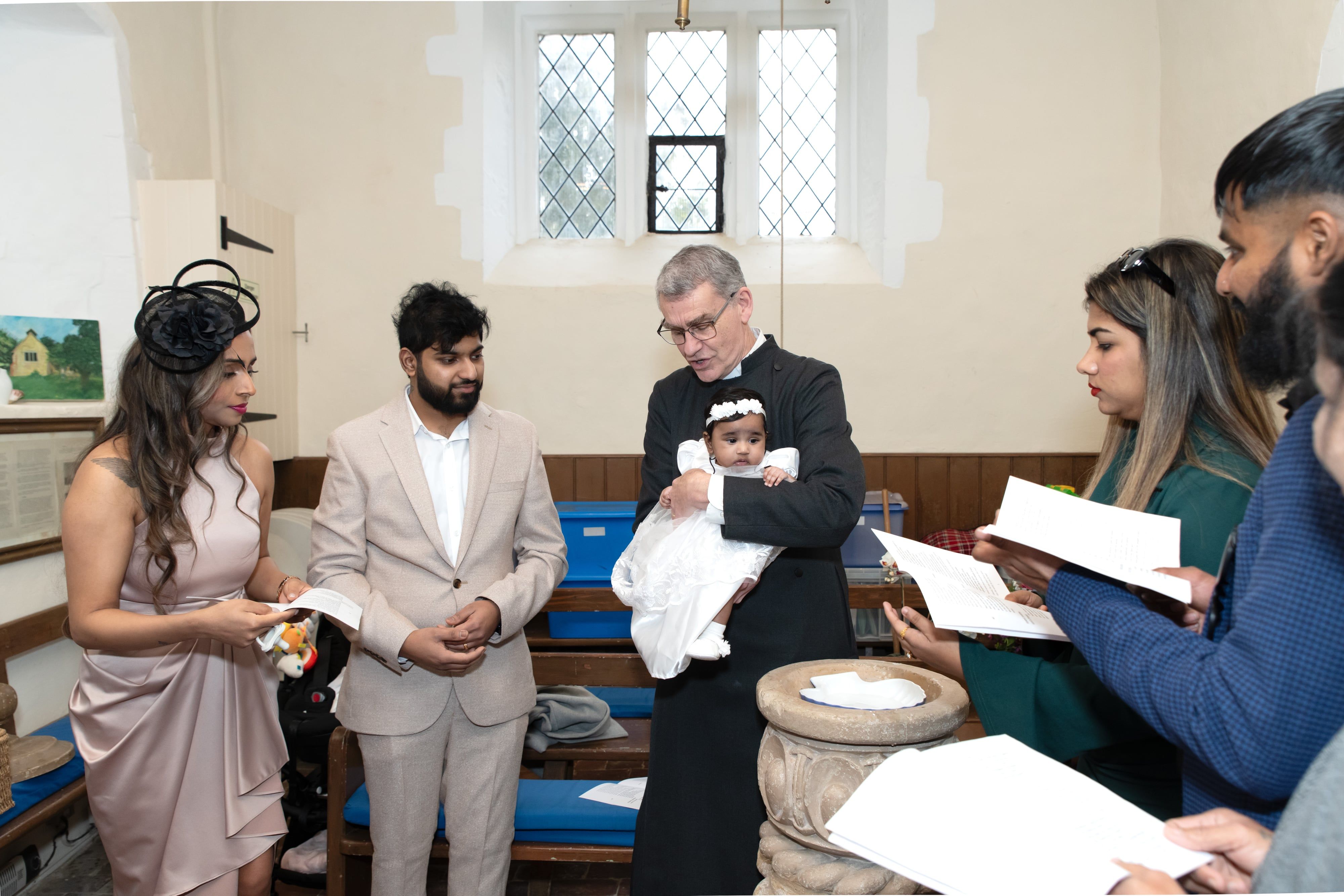 Vicar cradles the baby at the font as parents and godparents follow the order of service