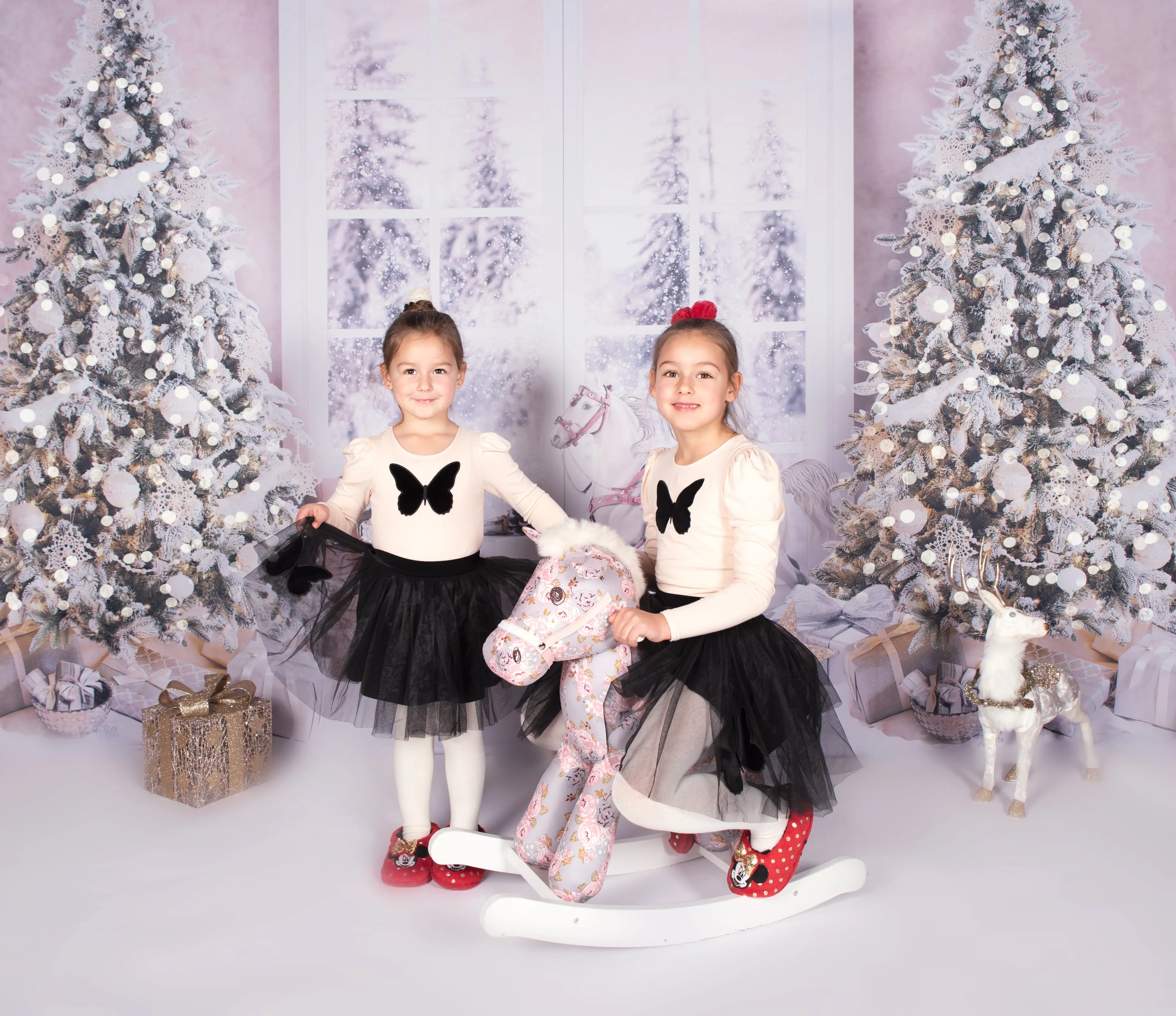 Mother and daughter laugh on red toy car in festive winter studio scene