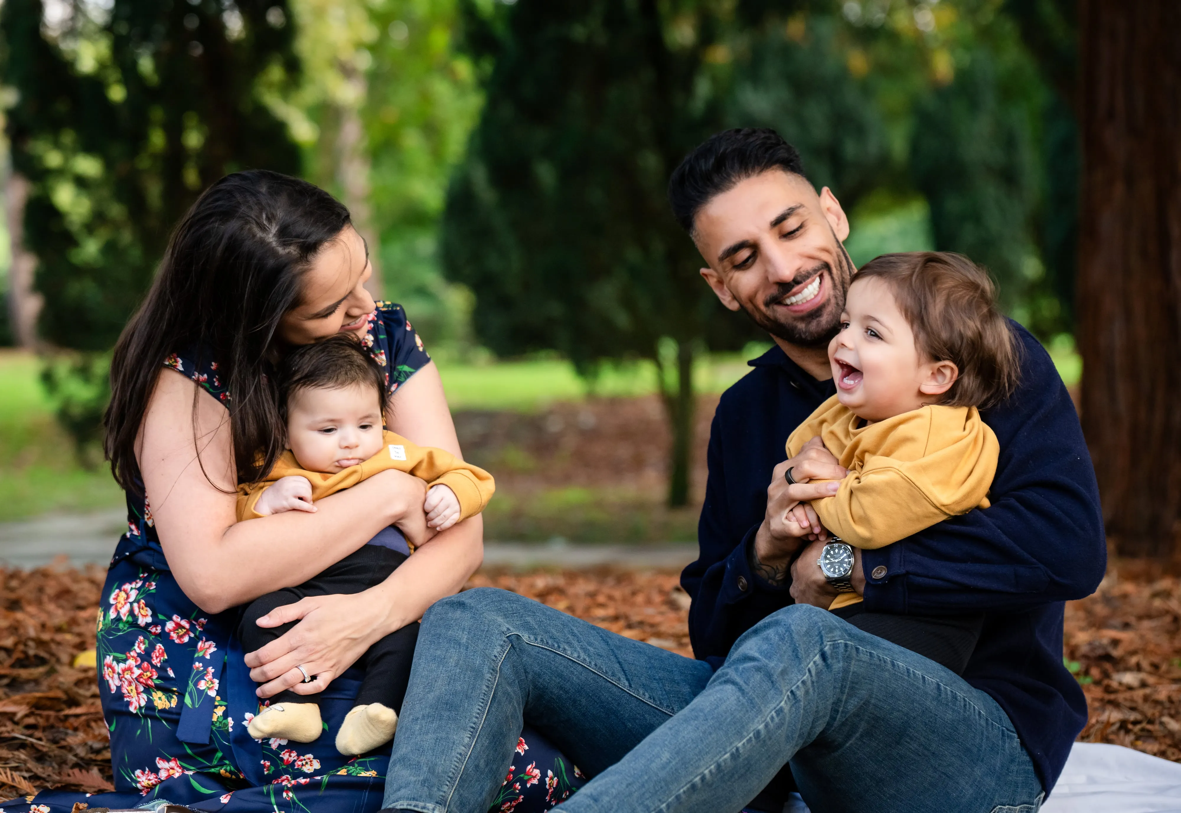 Parents laugh with two toddlers on an autumn picnic blanket