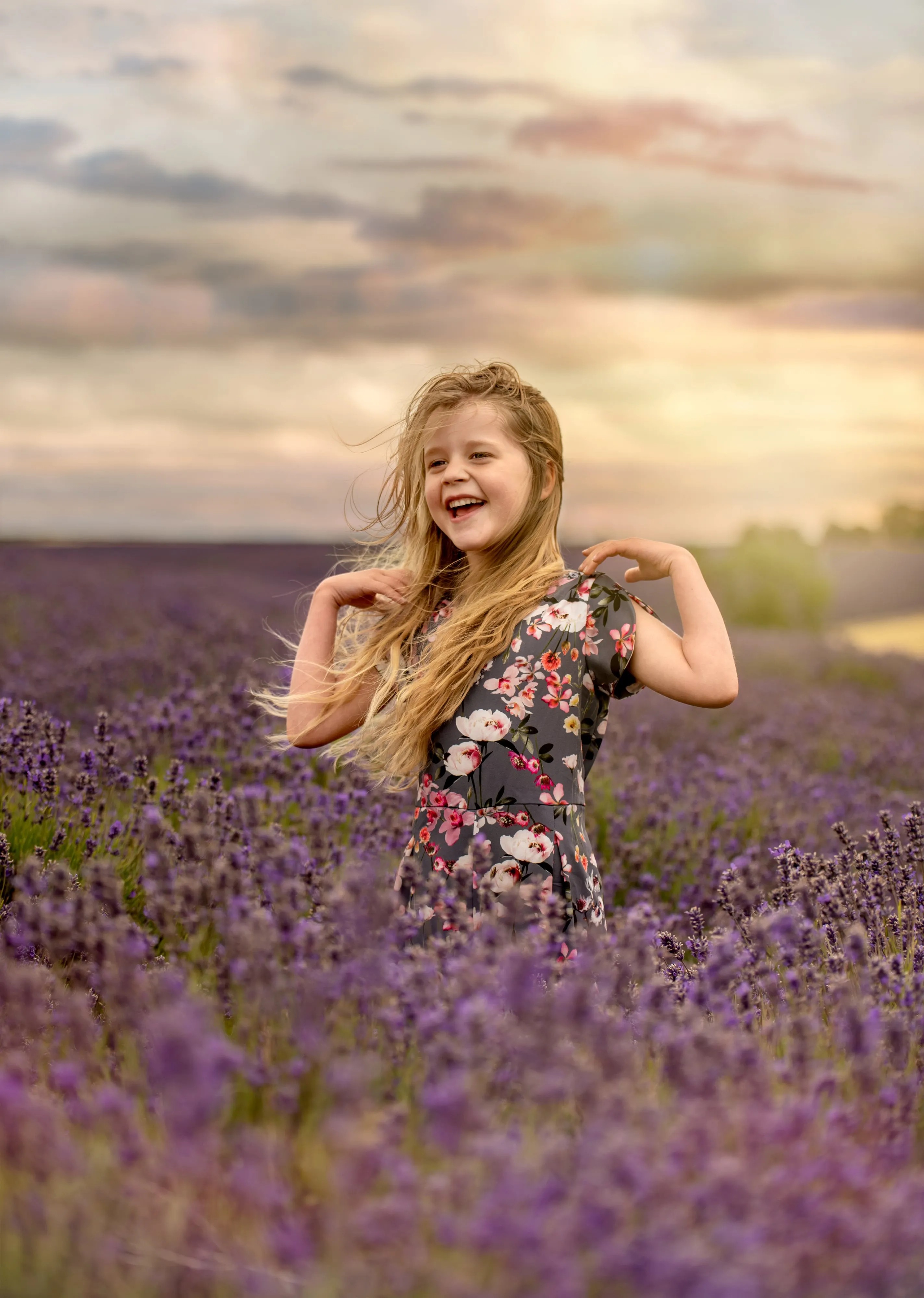 Long-haired girl laughs windblown in a lavender field at golden hour, soft cloudy sky overhead