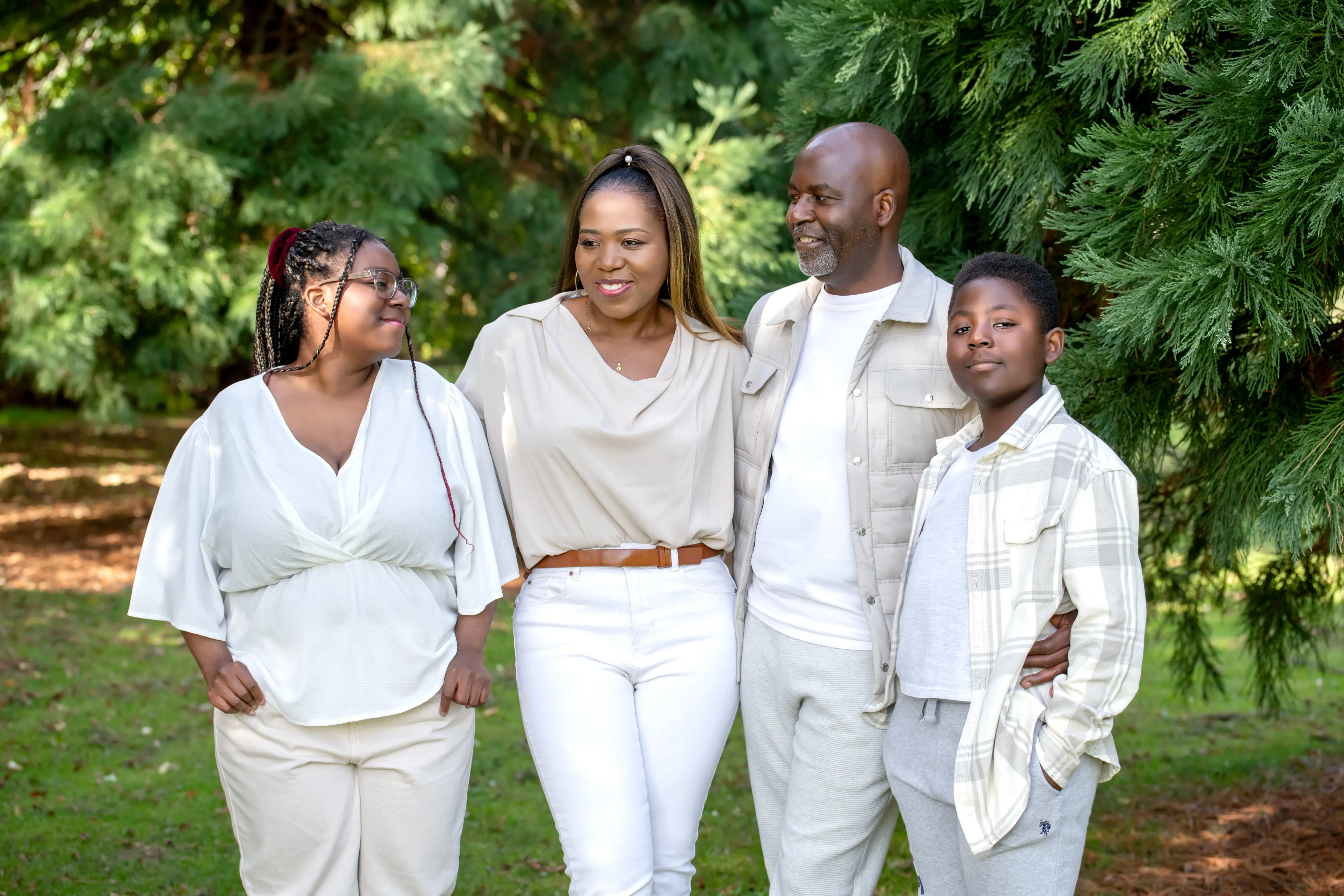 Family of four with two teenagers walk together in cream and beige outfits along a wooded parkland path