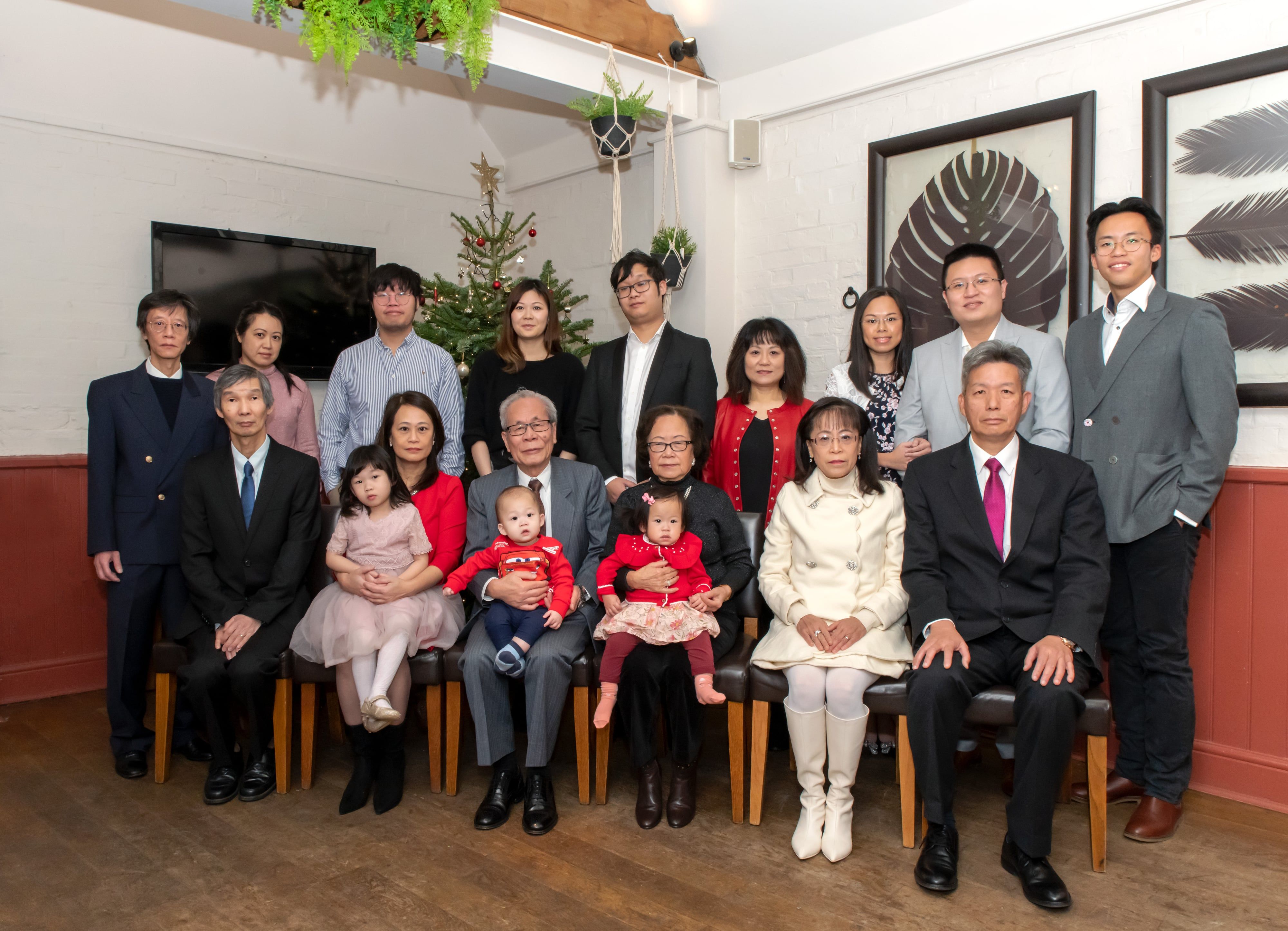 Three generations gathered for a family portrait beside a decorated Christmas tree at a festive party