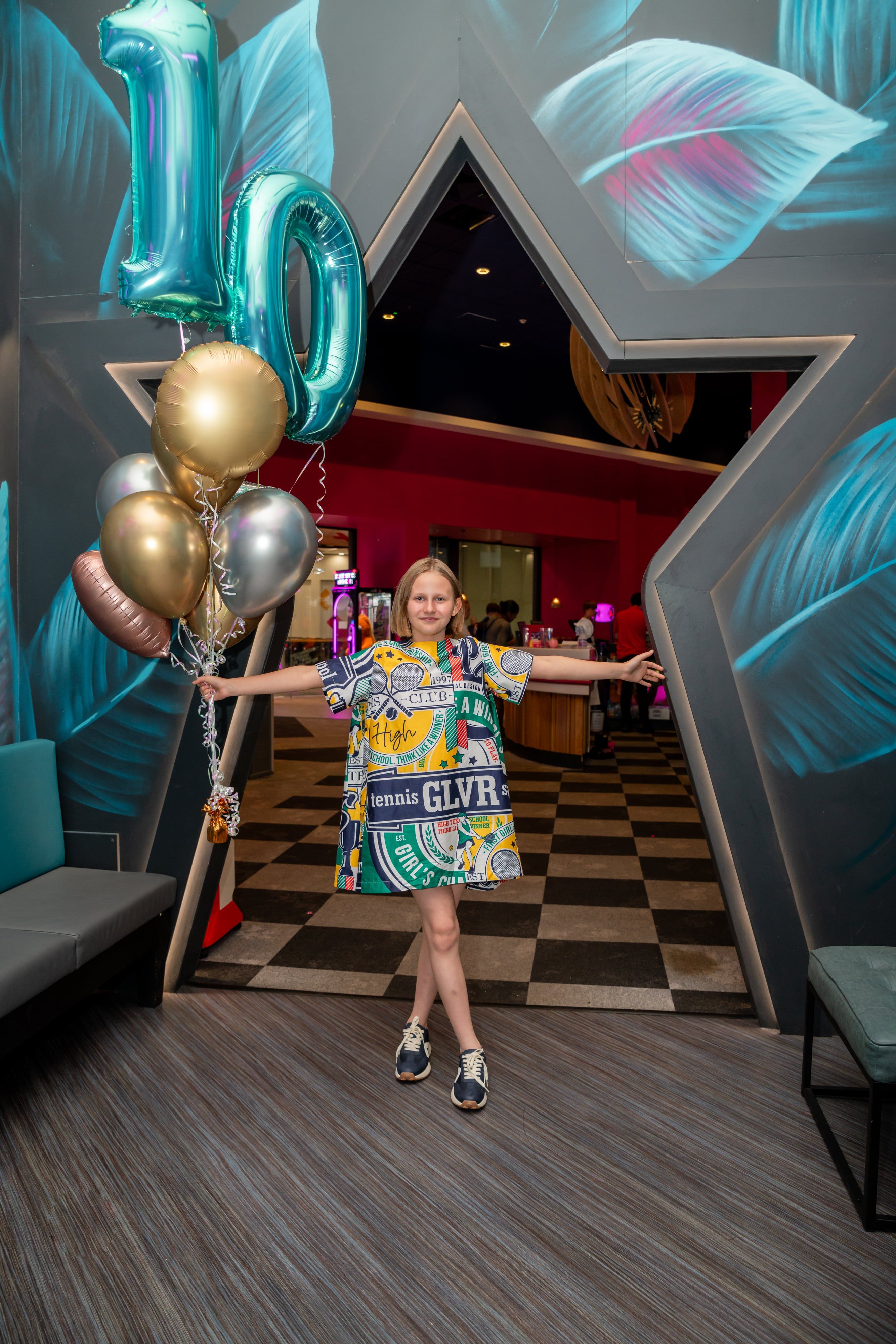 Girl flings her arms wide beside giant 10 balloons in the star-shaped doorway of a party venue