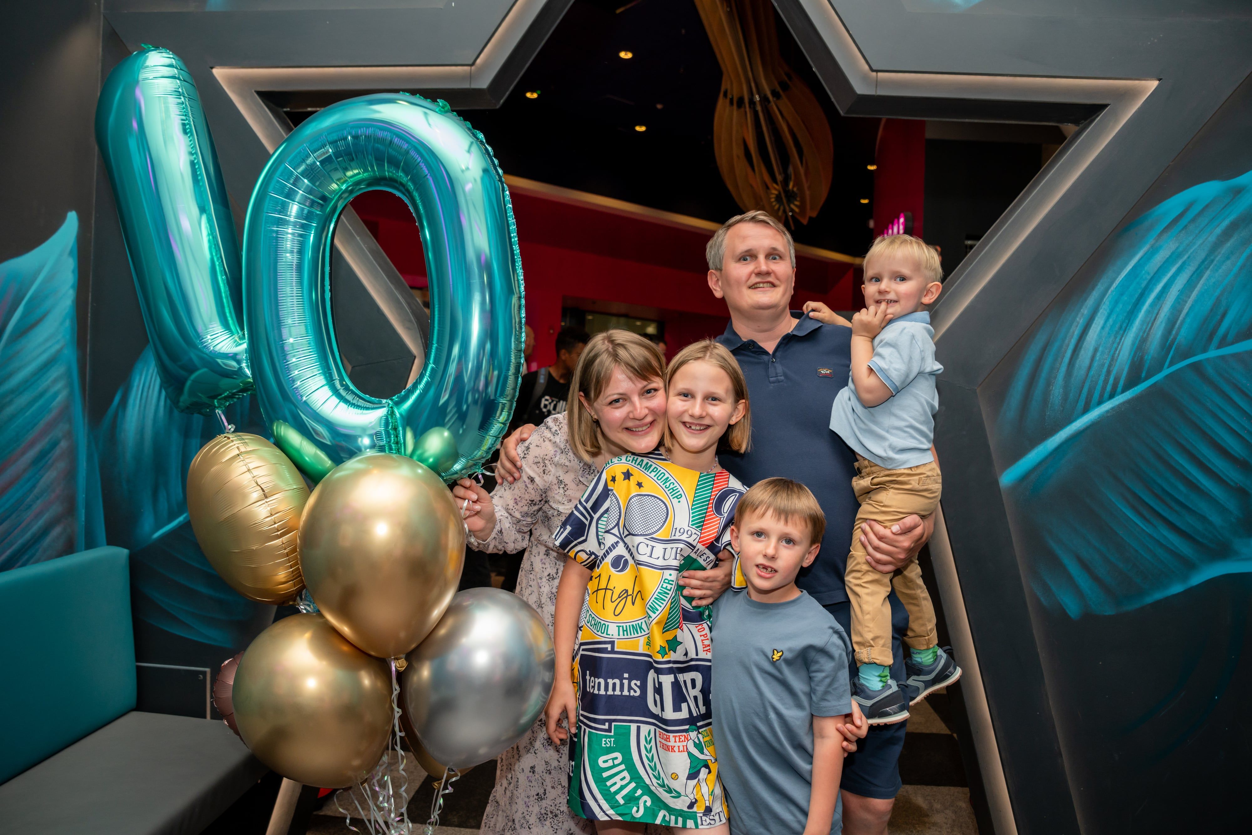 Family of five gathered around giant 10 balloons at a tenth-birthday party venue