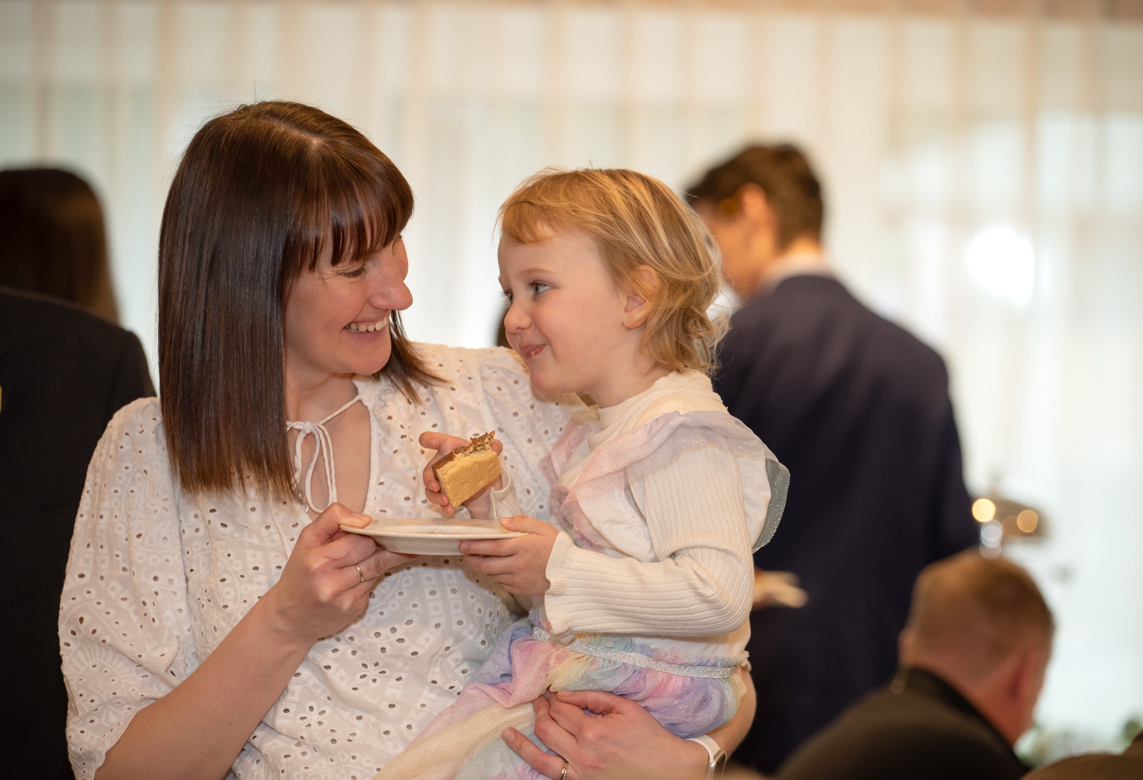 Mother smiles with her toddler as the little one tucks into a slice of cake