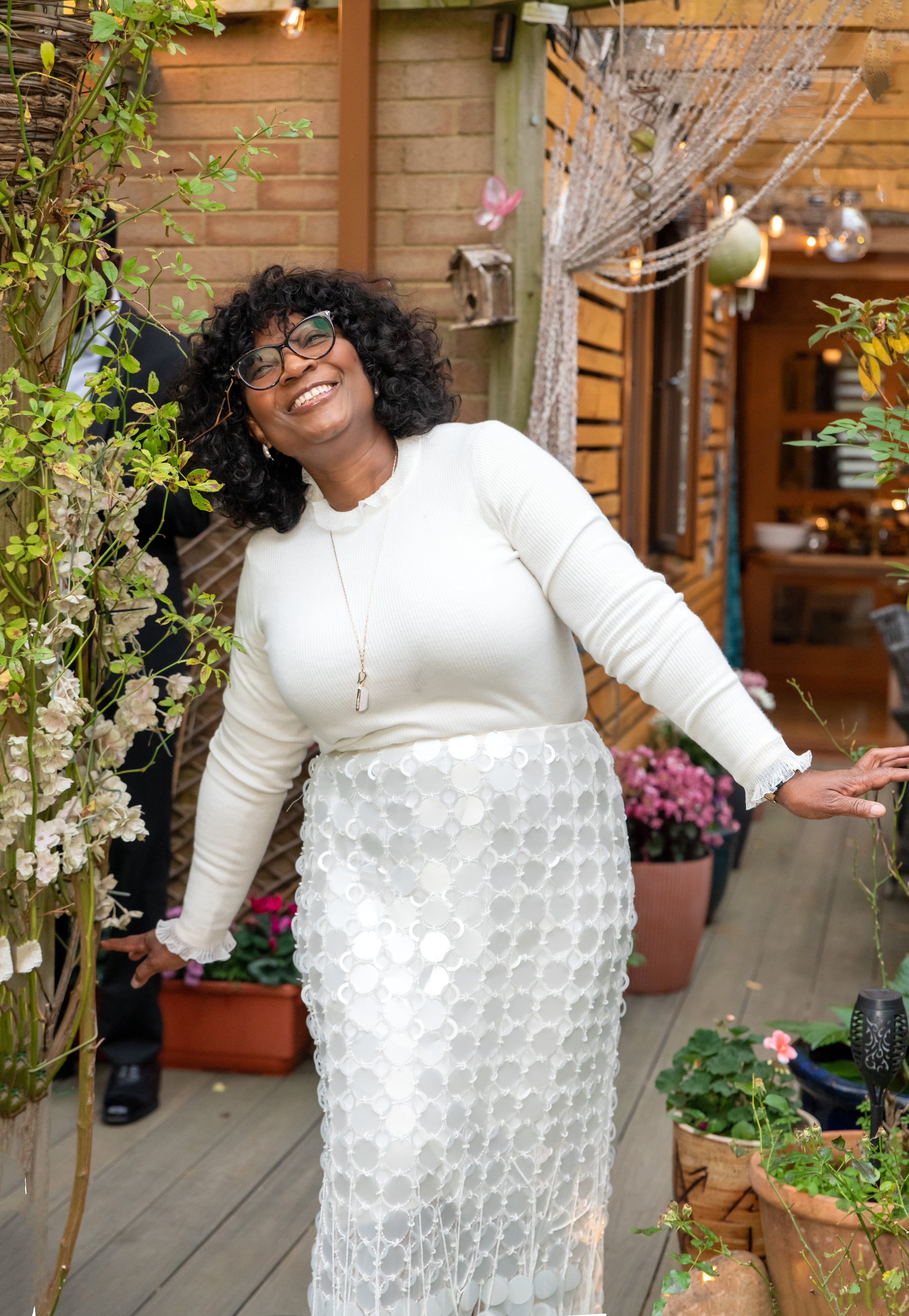 Guest in a white sequinned skirt laughs among the flowers on the garden decking