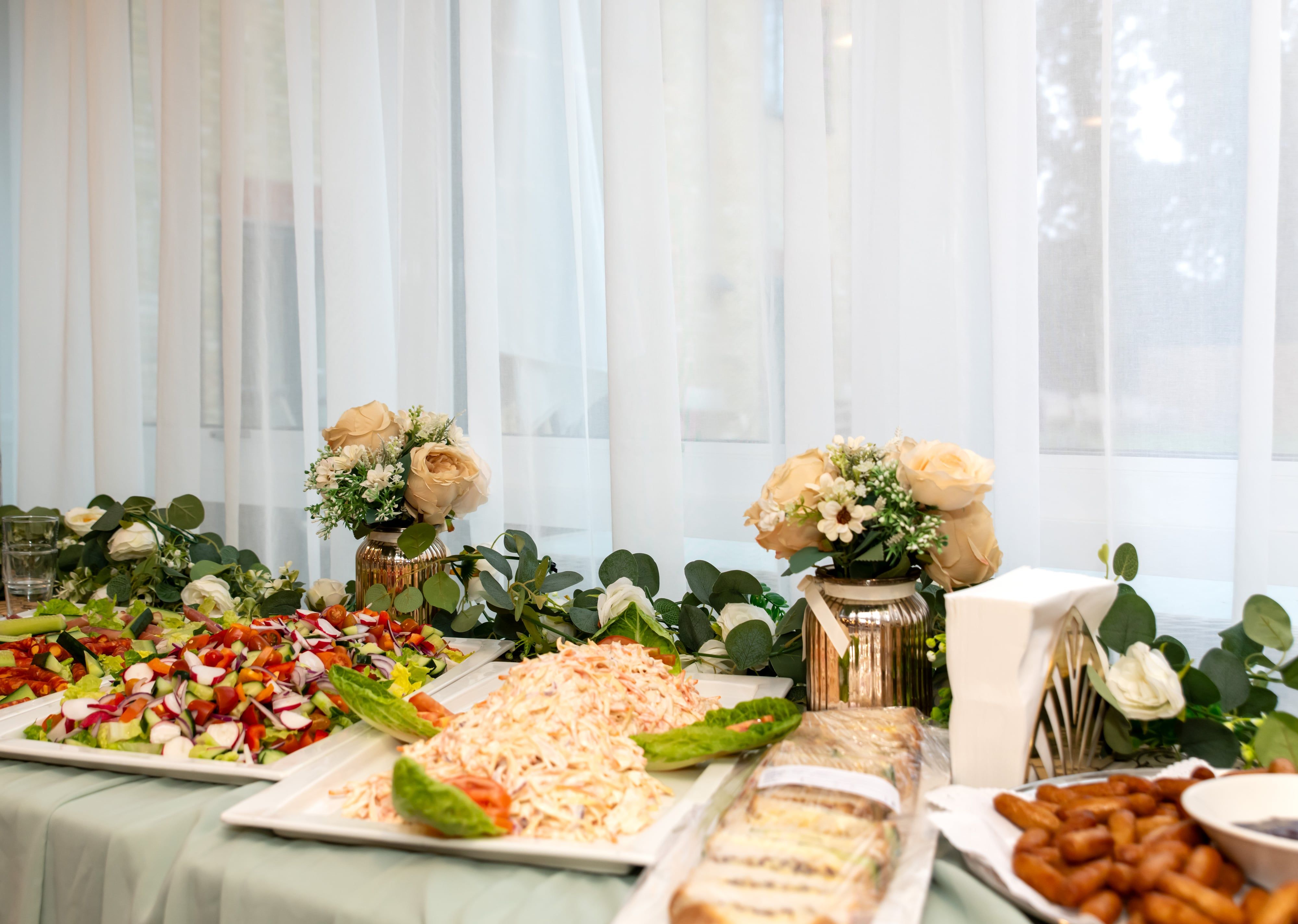 Celebration buffet table laid with salads, sandwiches and flowers by a sunlit window