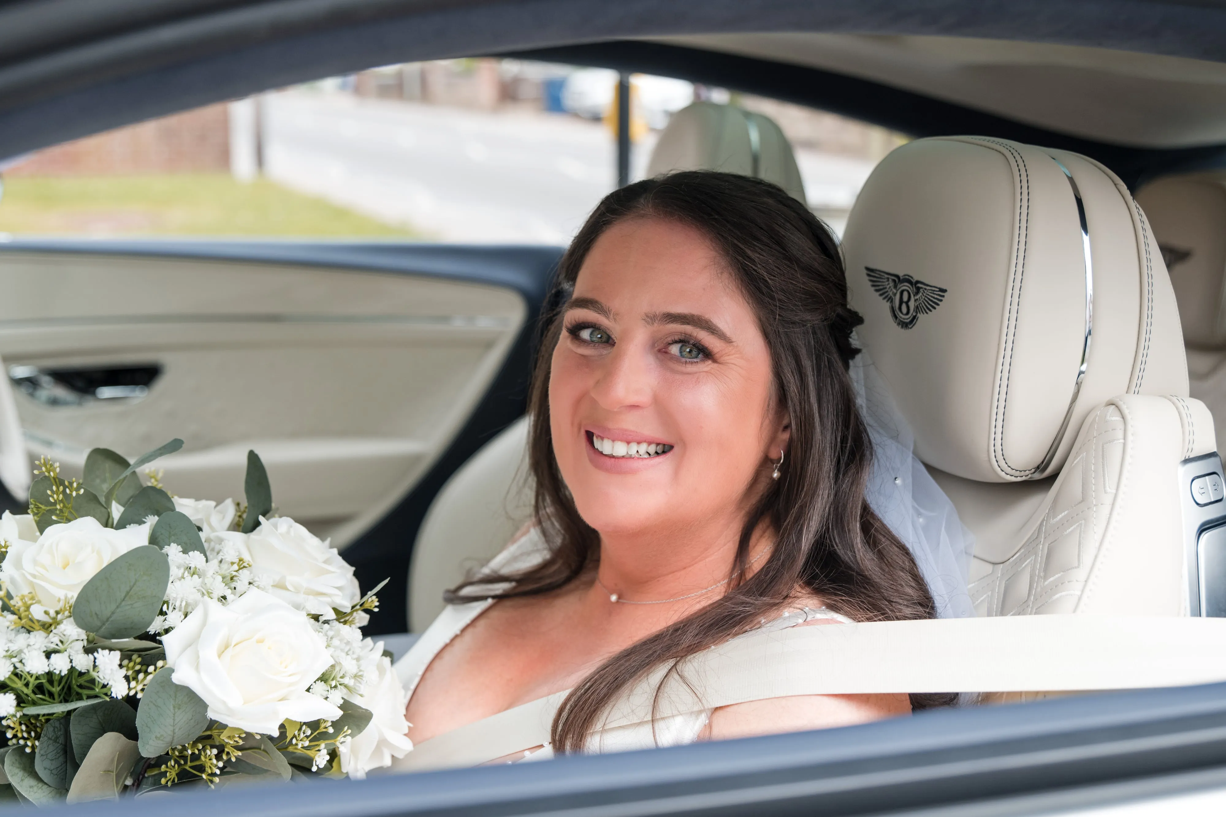 Bride smiles in white Bentley wedding car arriving at the Belfry