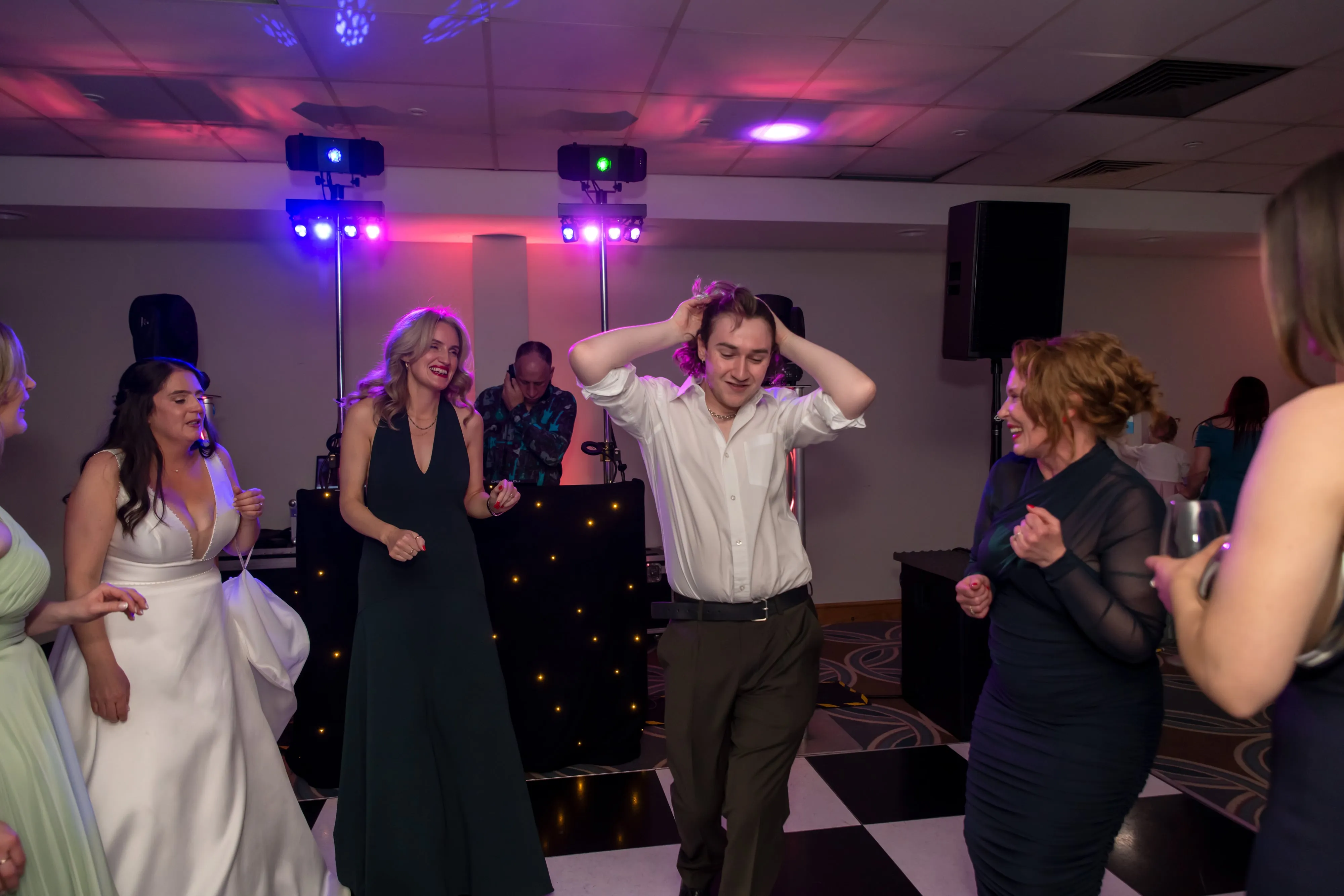 Bride and groom dance with guests under disco lights at Belfry evening reception