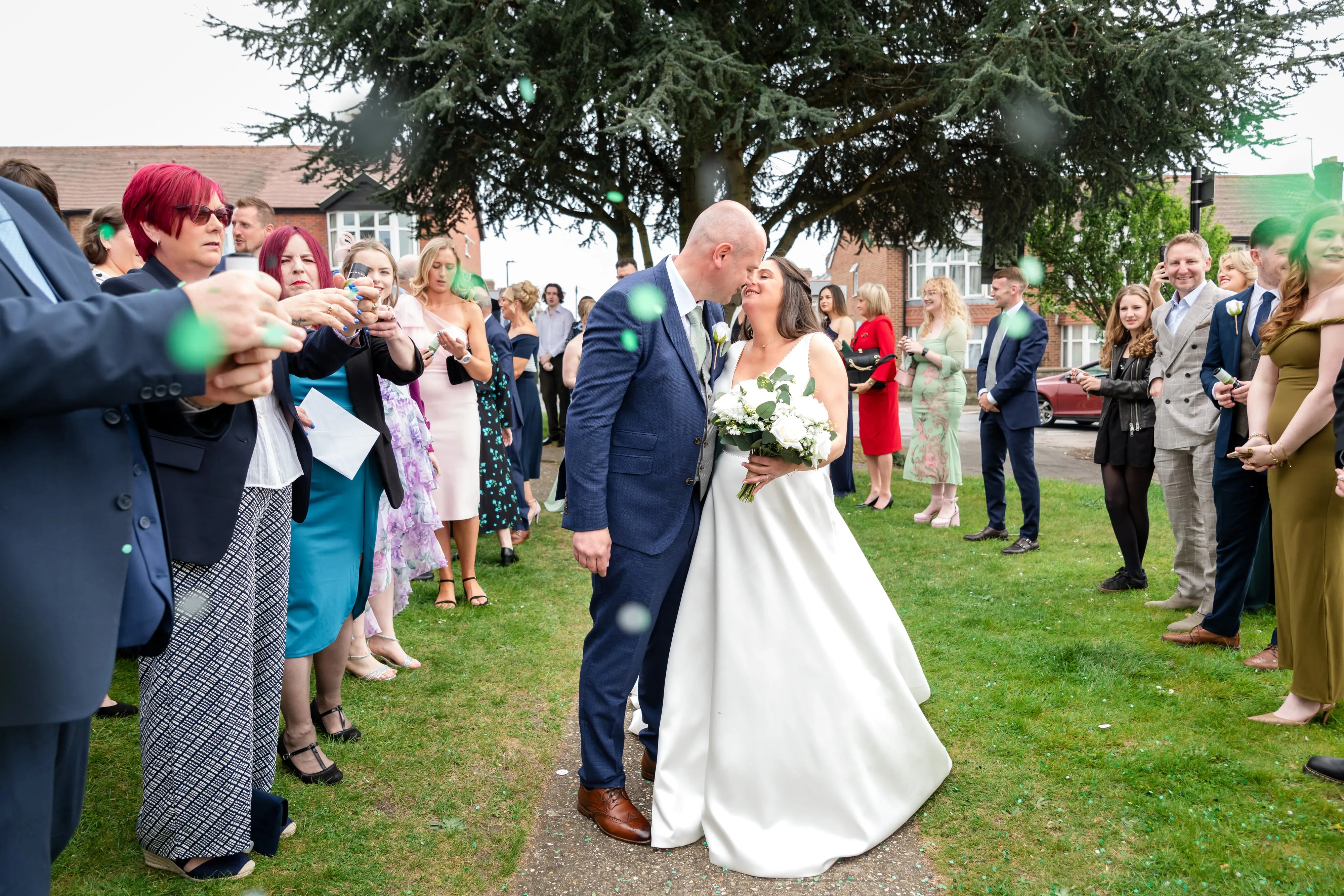 Bride and groom share kiss in confetti shower under cedar tree at The Oxford Belfry Hotel & Spa