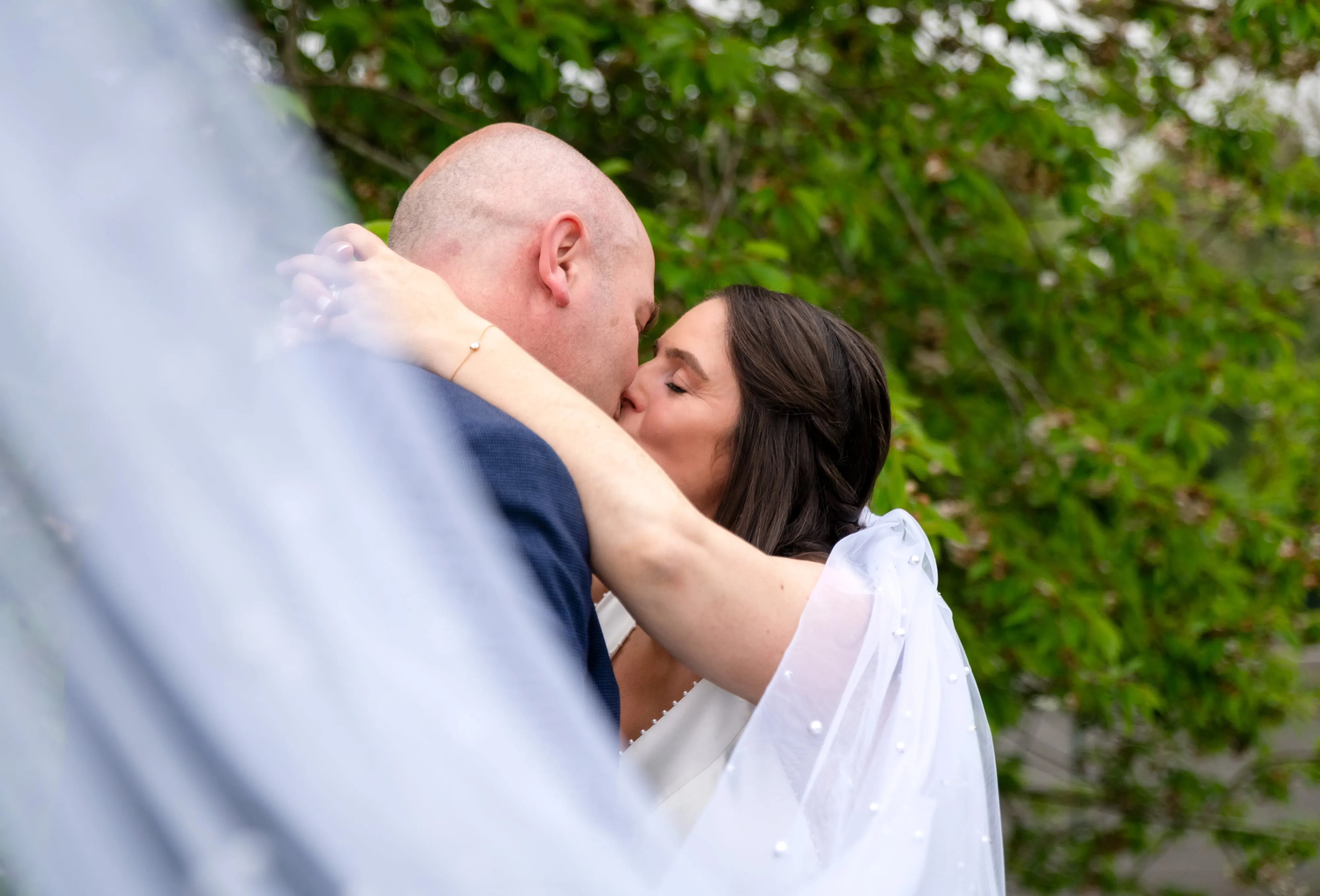 Bride and groom kiss tenderly with veil framing intimate Belfry garden moment