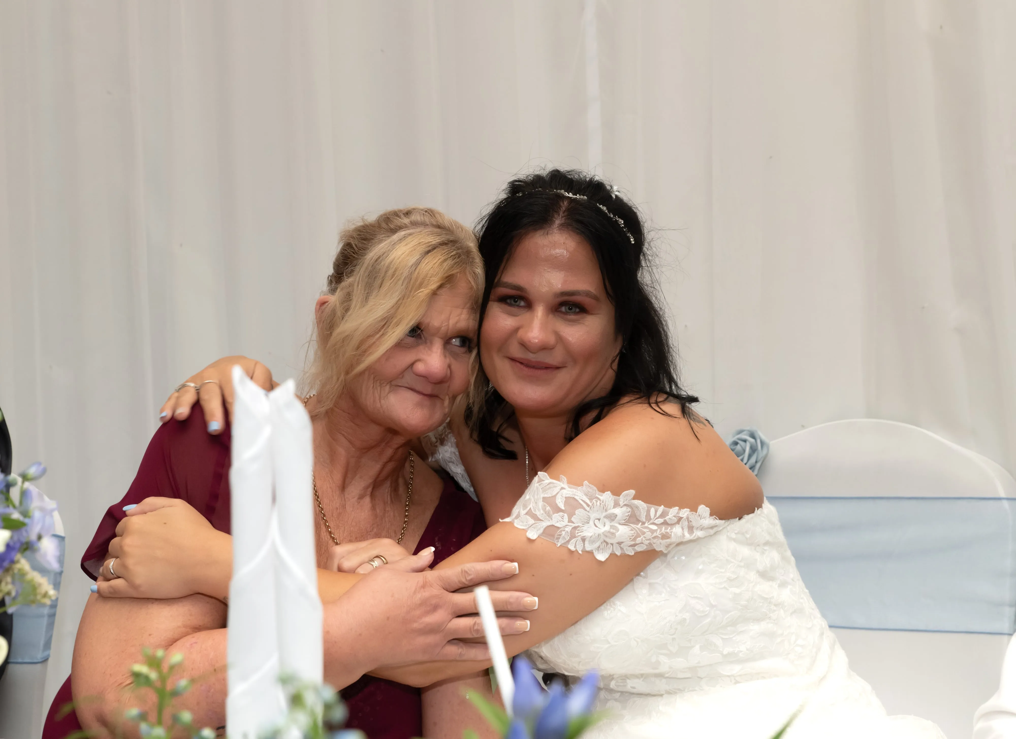 Bride embraces her mother at the reception, an intimate cheek-to-cheek moment behind the top-table florals