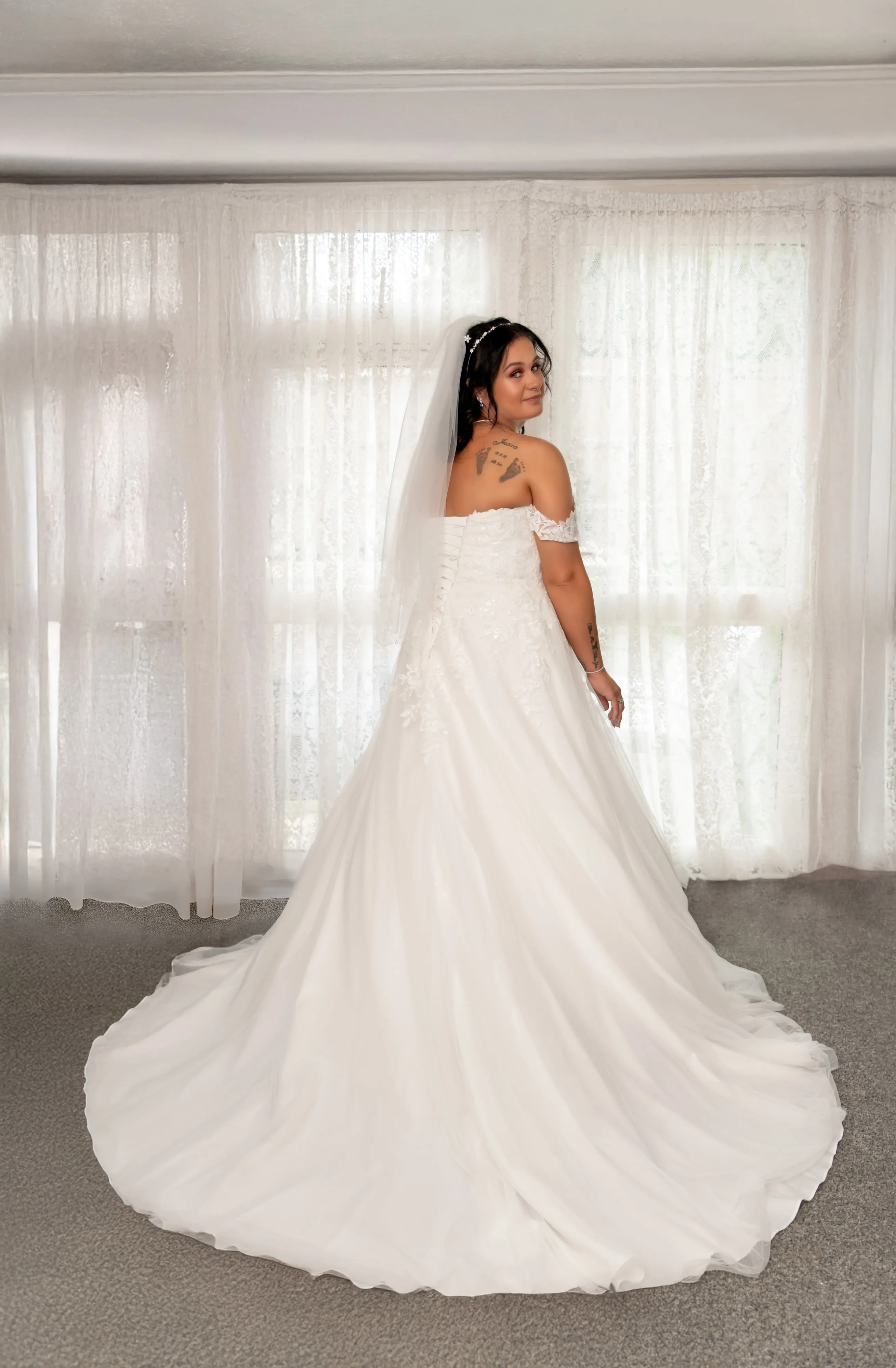 Bride photographed from behind in lace ballgown with sweeping train against tall lace curtains