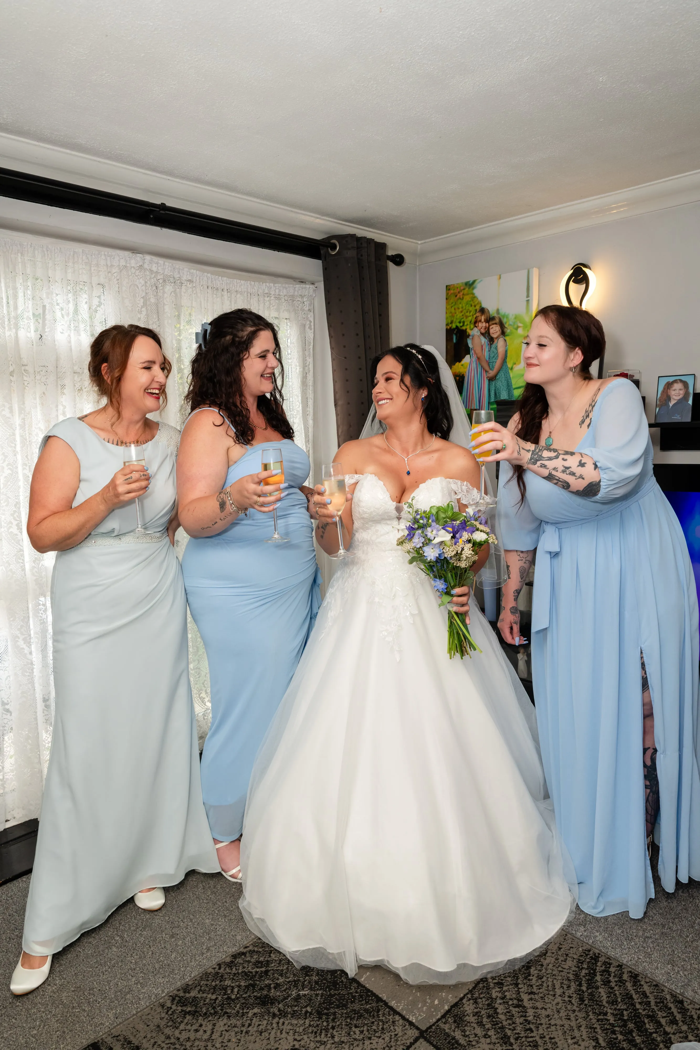 Bride raises her bouquet for a champagne toast with three bridesmaids in pale-blue gowns