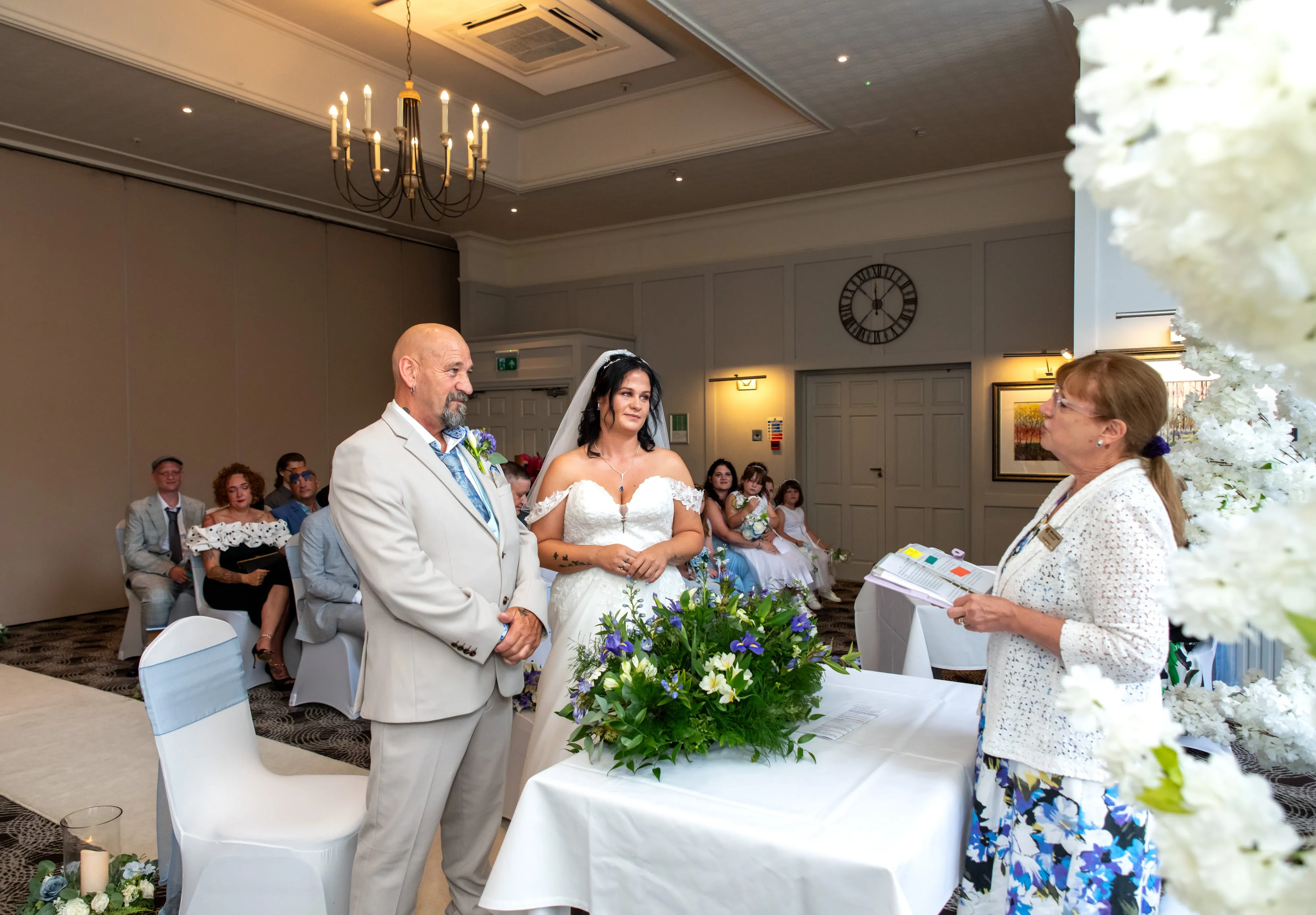 Wide view of the civil ceremony with bride, groom, celebrant and guests under a chandelier at Holiday Inn Milton Keynes East