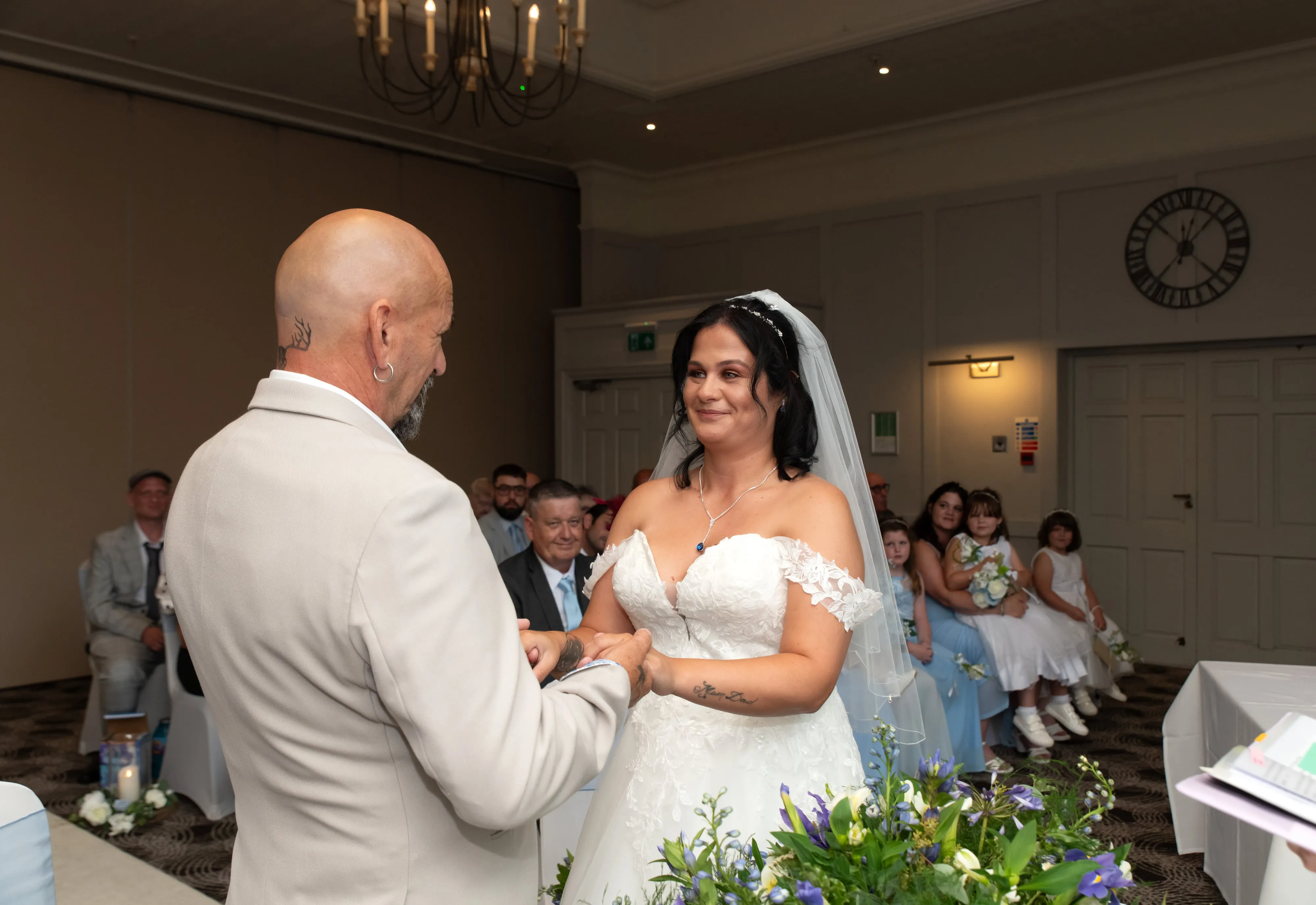 Bride and groom exchange smiles during the vow exchange under a Holiday Inn chandelier