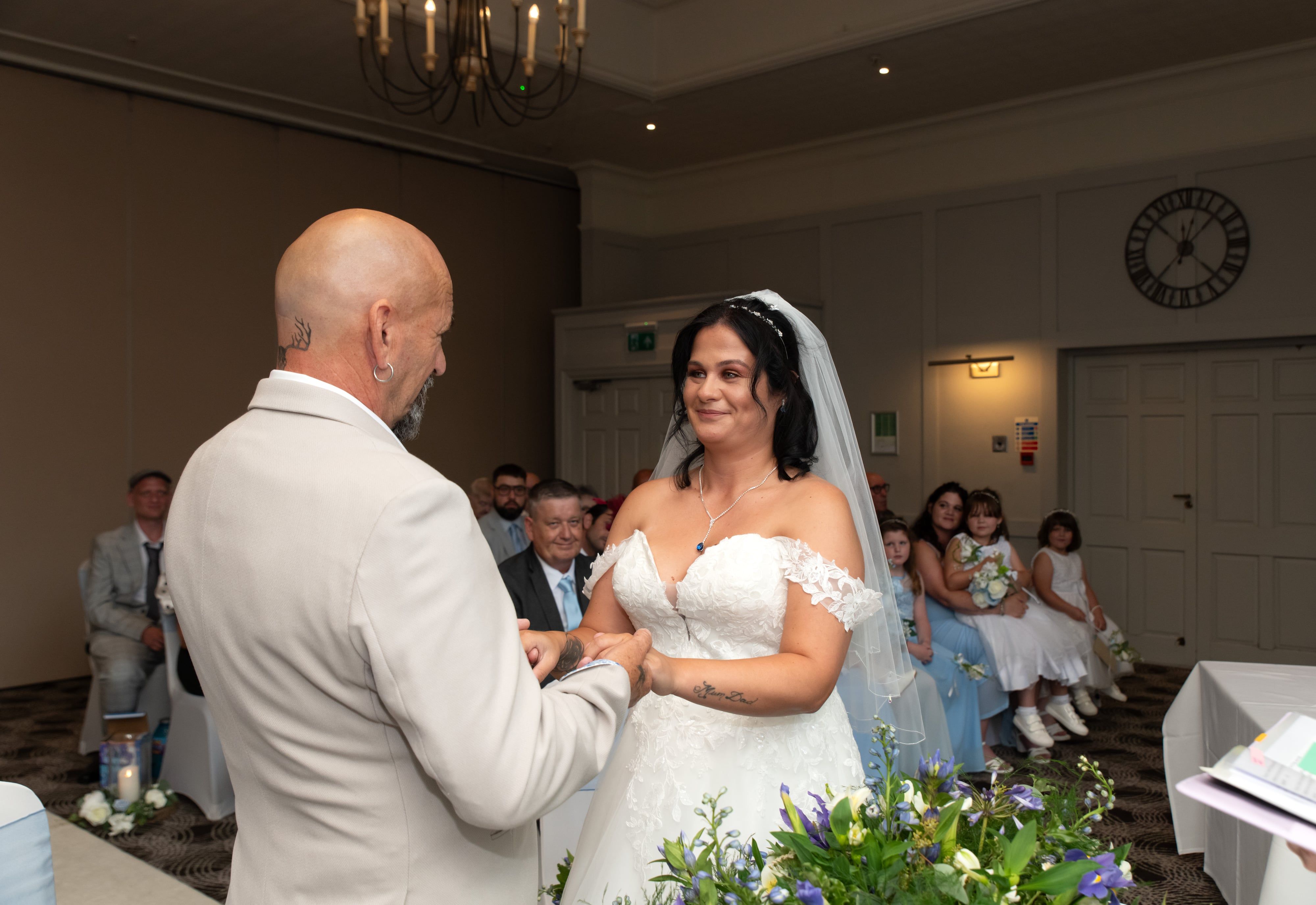 Bride and groom exchange smiles during the vow exchange under a Holiday Inn chandelier