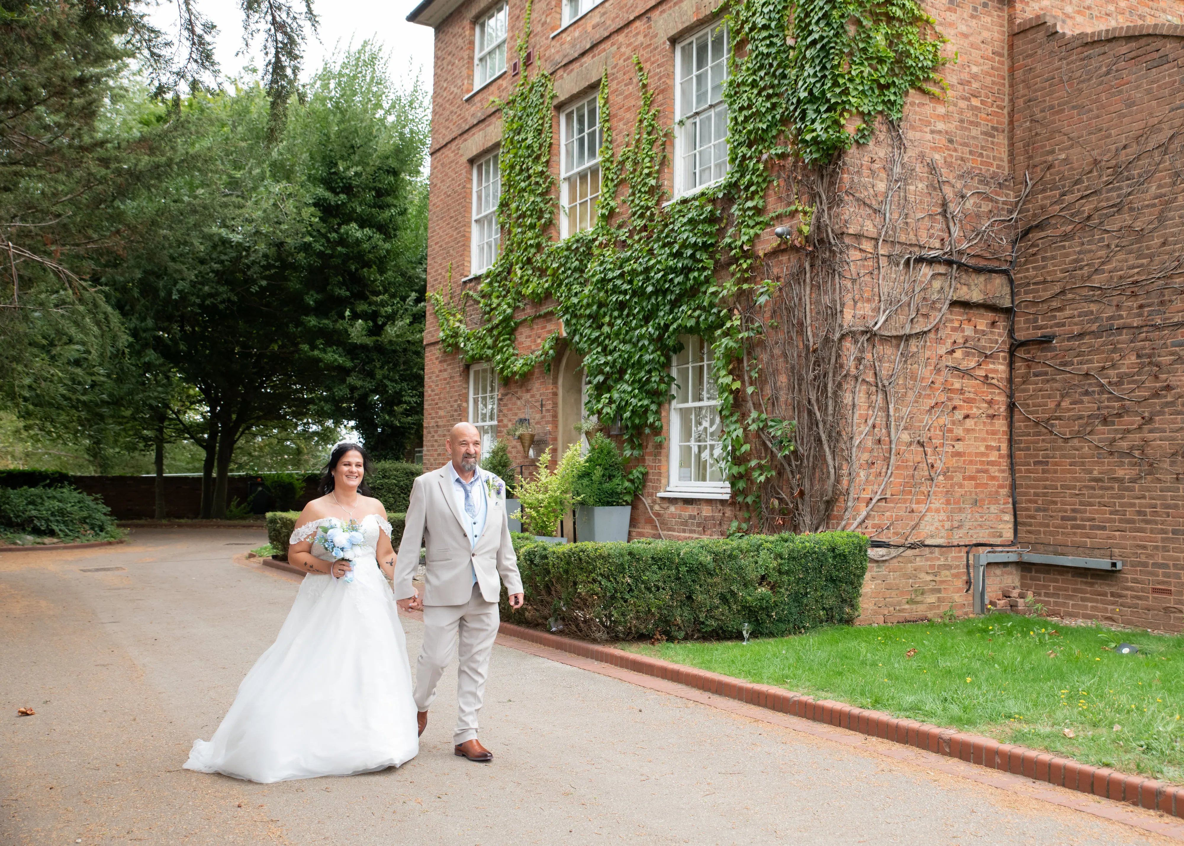 Bride and groom walk hand in hand past the ivy-covered red brick wedding venue