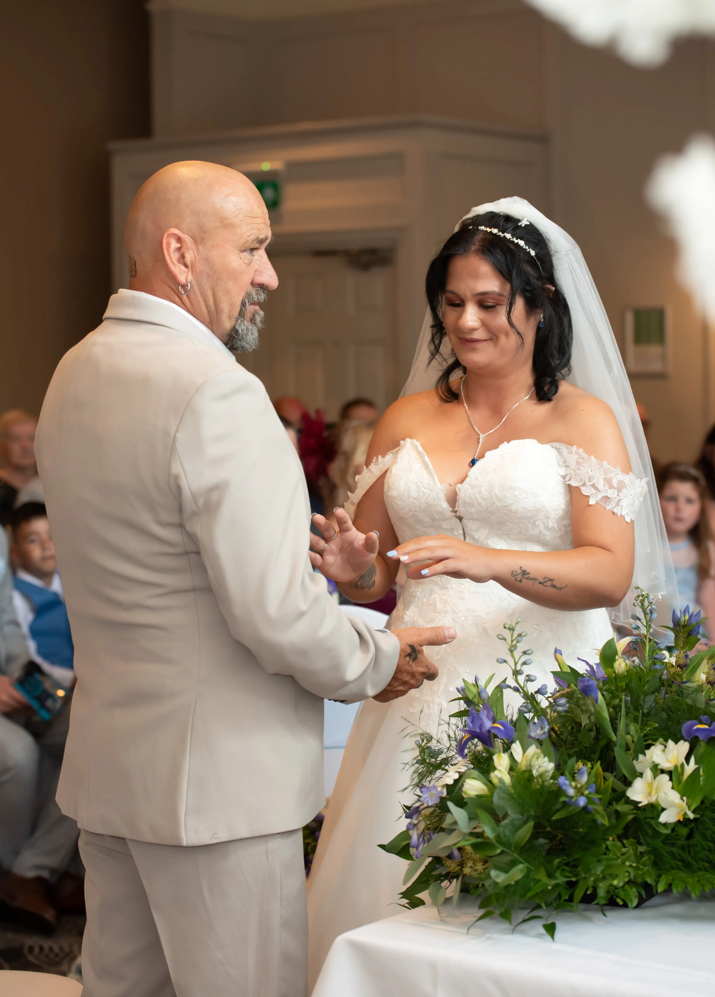 Bride and groom exchange rings during the vow exchange, bouquet of irises and wildflowers in foreground