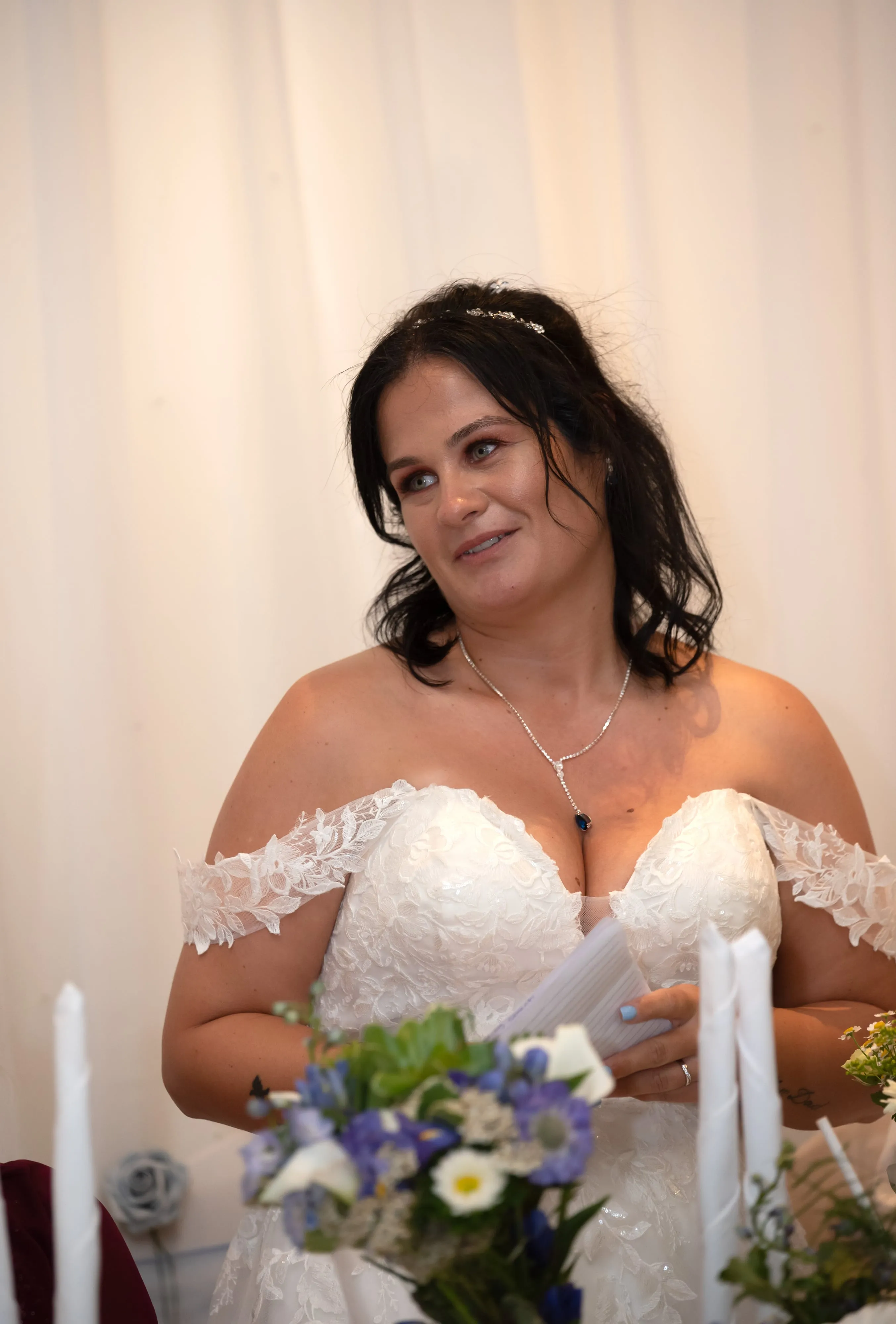Bride listens to a wedding speech, holding her notes above a bouquet of irises and wildflowers