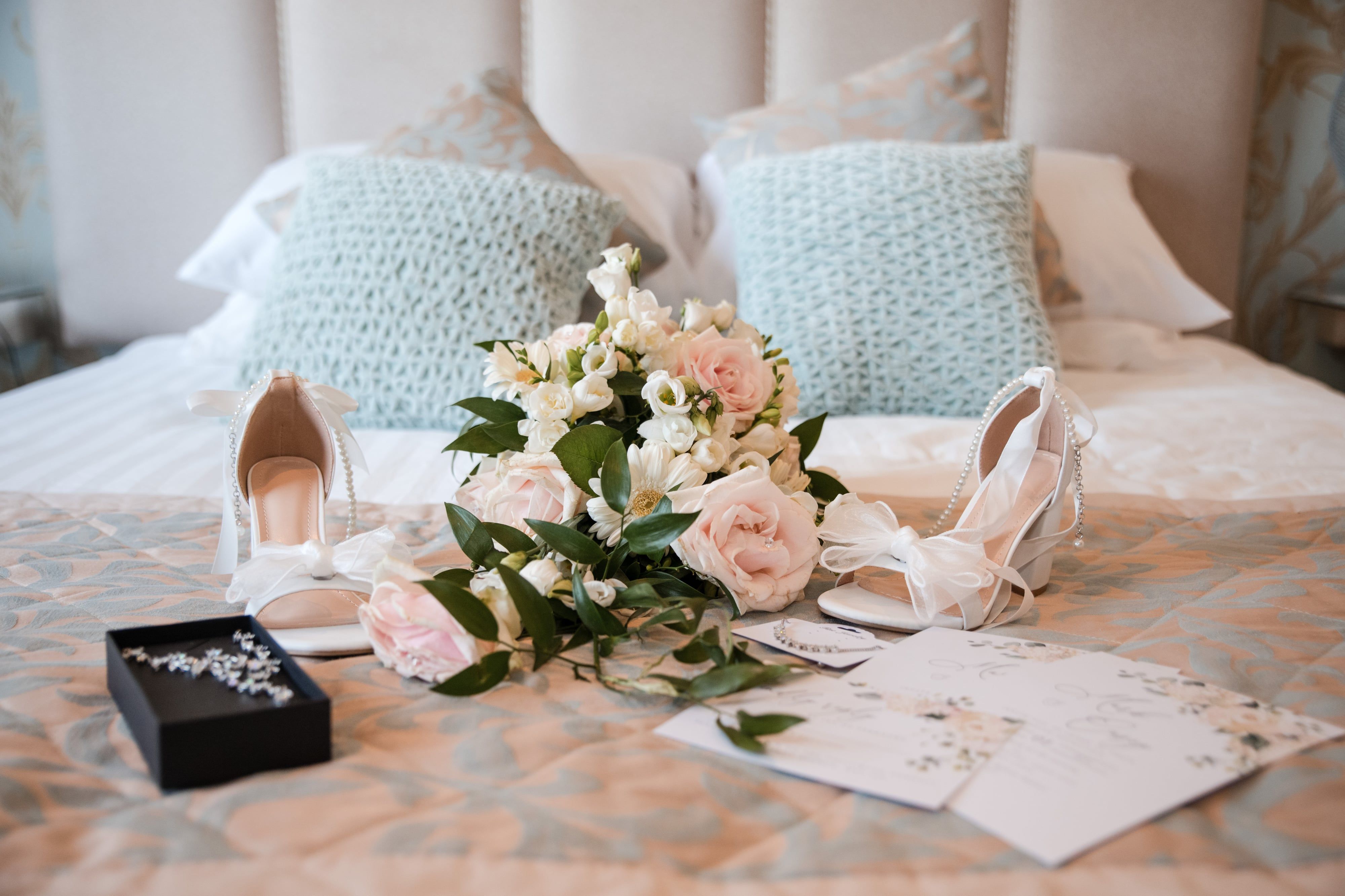 Bridal heels, blush rose bouquet and jewellery box laid out on the hotel bed before the ceremony