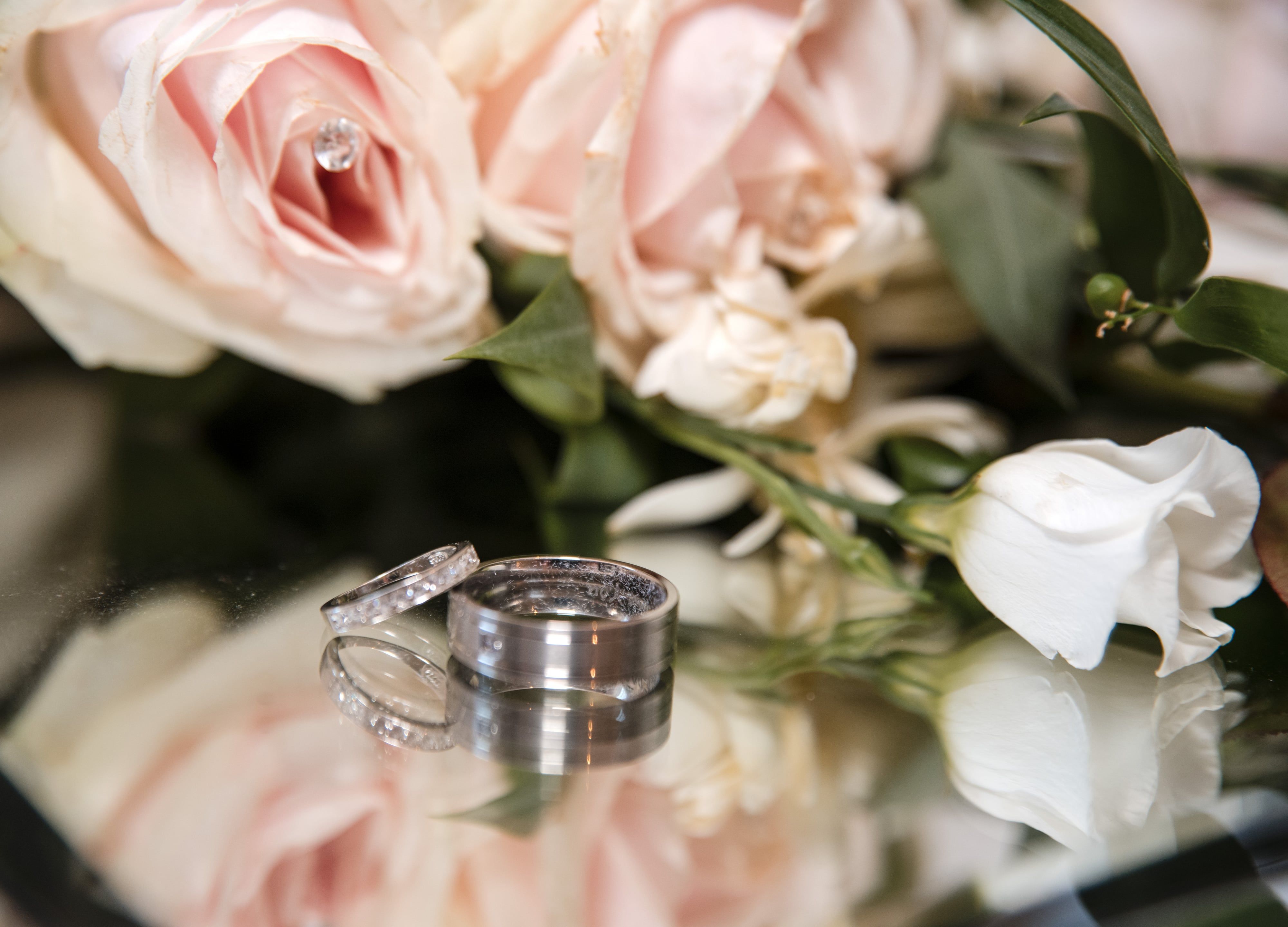 Wedding rings resting on a mirrored surface beside blush roses