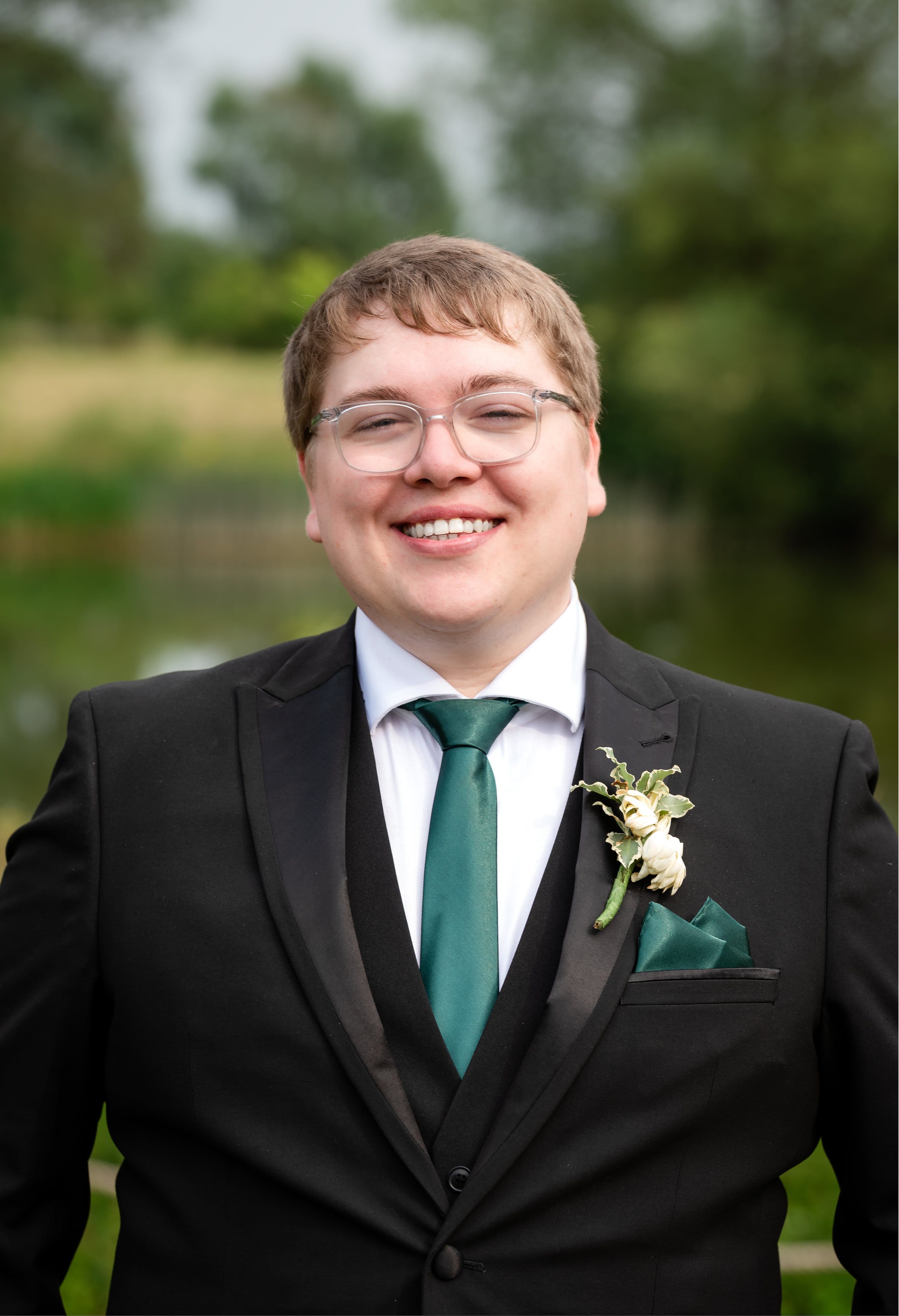 Groom portrait in black suit and green tie by the lake