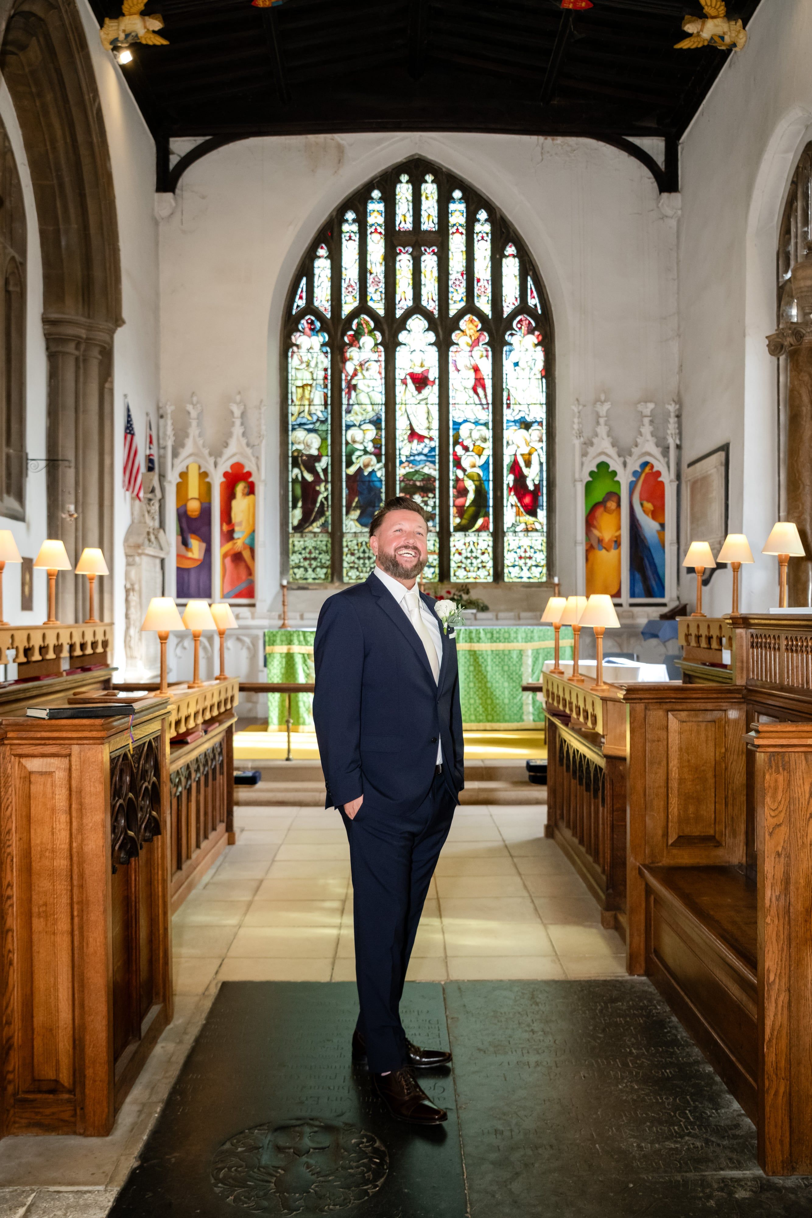 Groom waits in the chancel of St Andrew's Church, Ampthill, beneath the beamed roof and stained glass