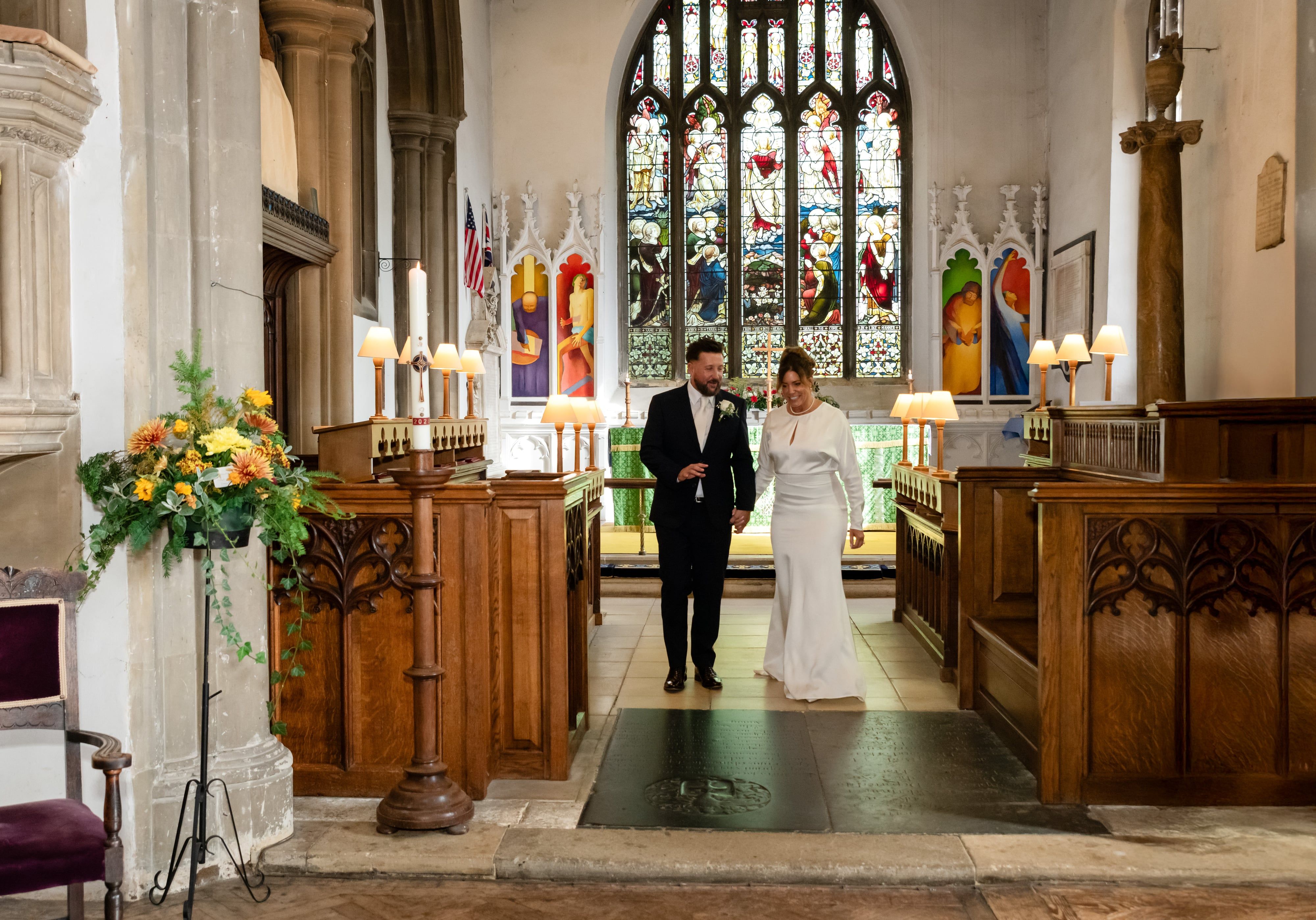 Newlyweds walk hand in hand from the chancel past autumn flowers and carved oak choir stalls