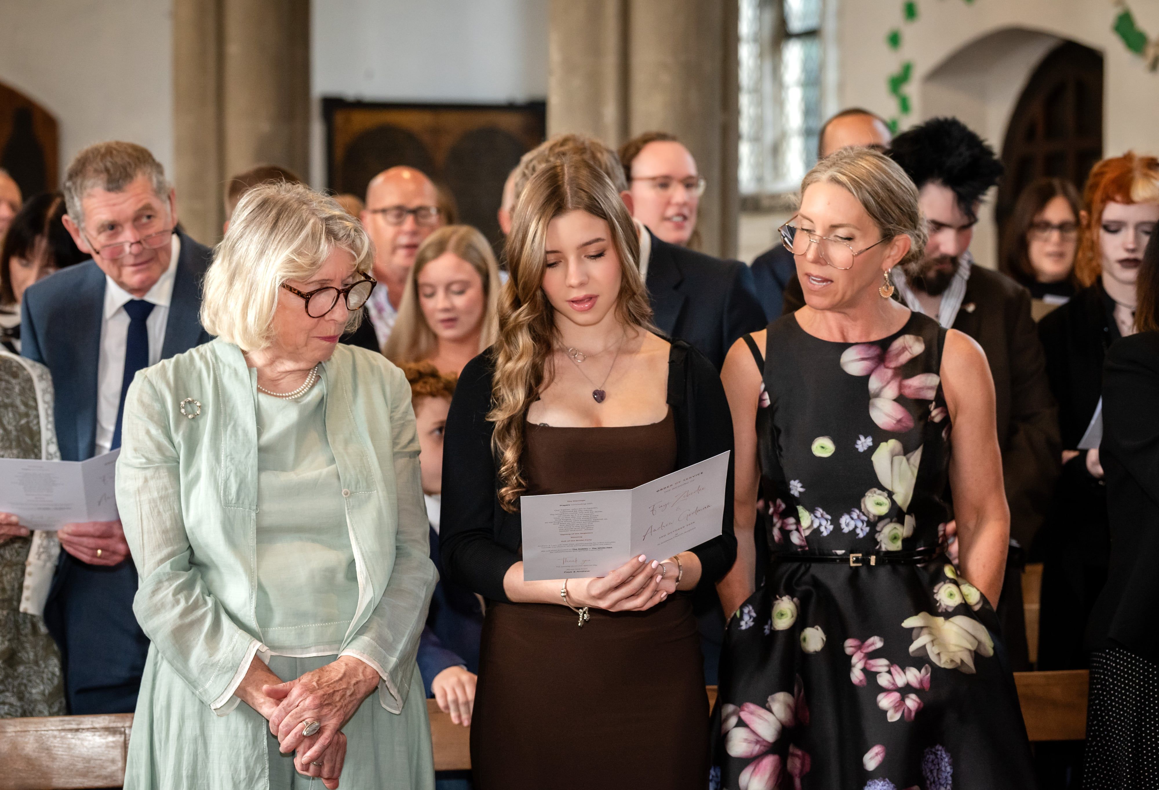 Wedding guests stand in the pews of St Andrew's Church, Ampthill, singing a hymn from the order of service