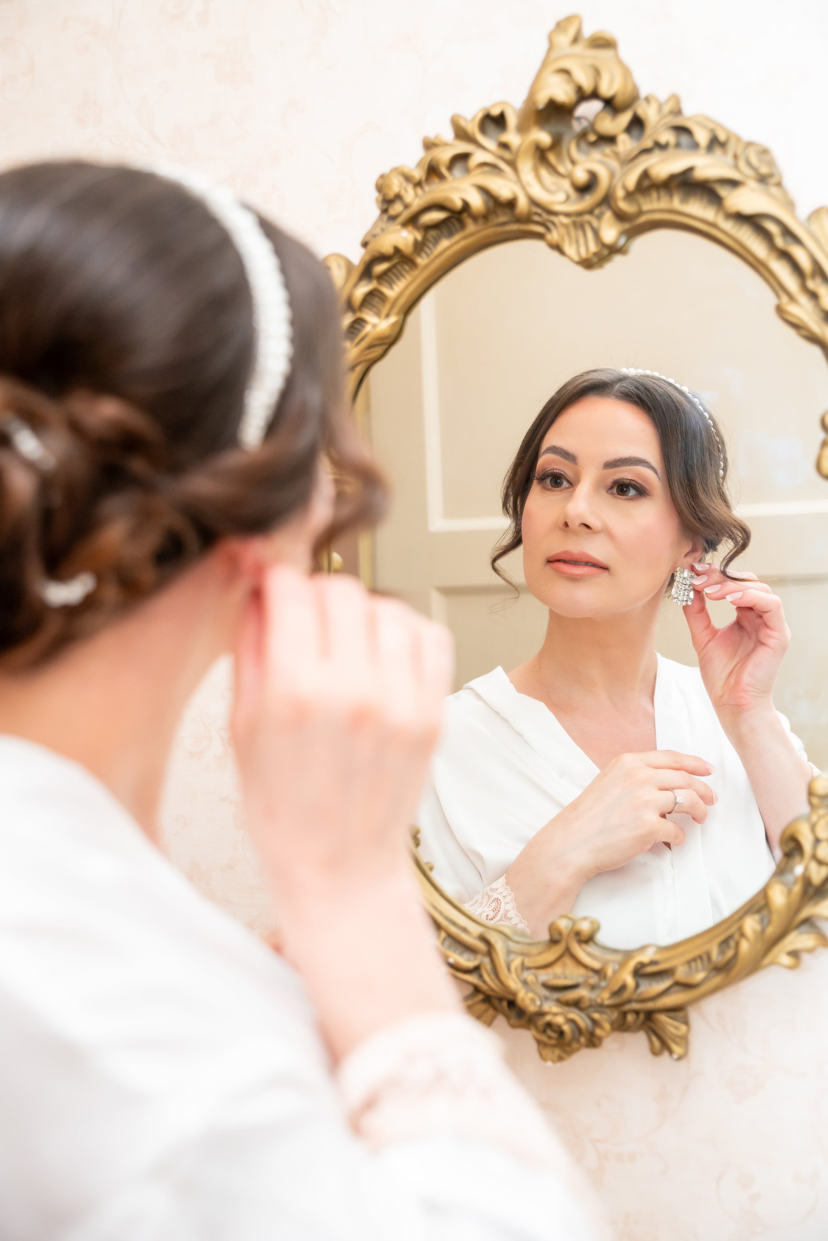Bride fixes her earring in a gold-framed mirror during the morning preparations