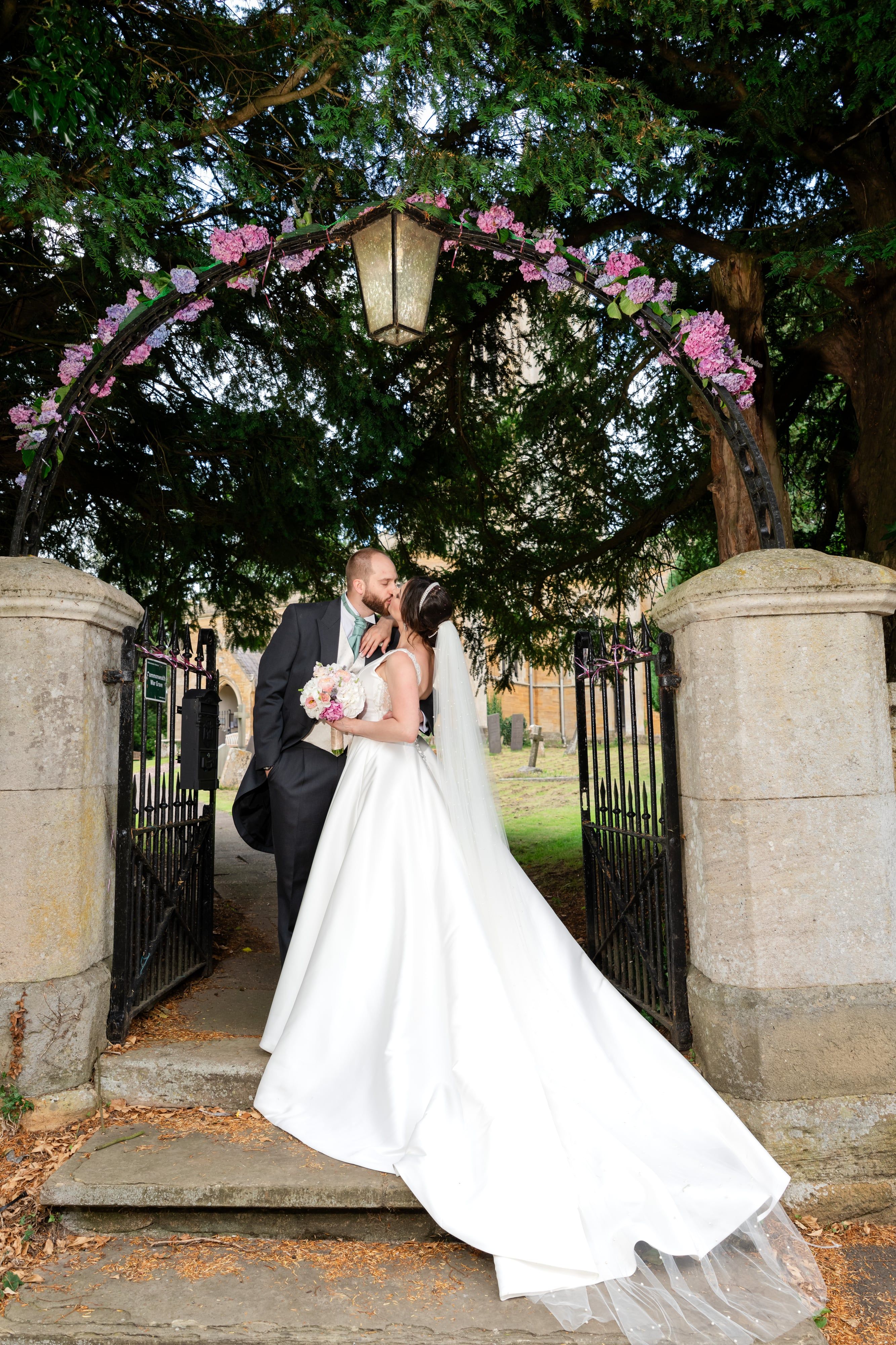 Kiss beneath the flower-arched lantern gate of the churchyard