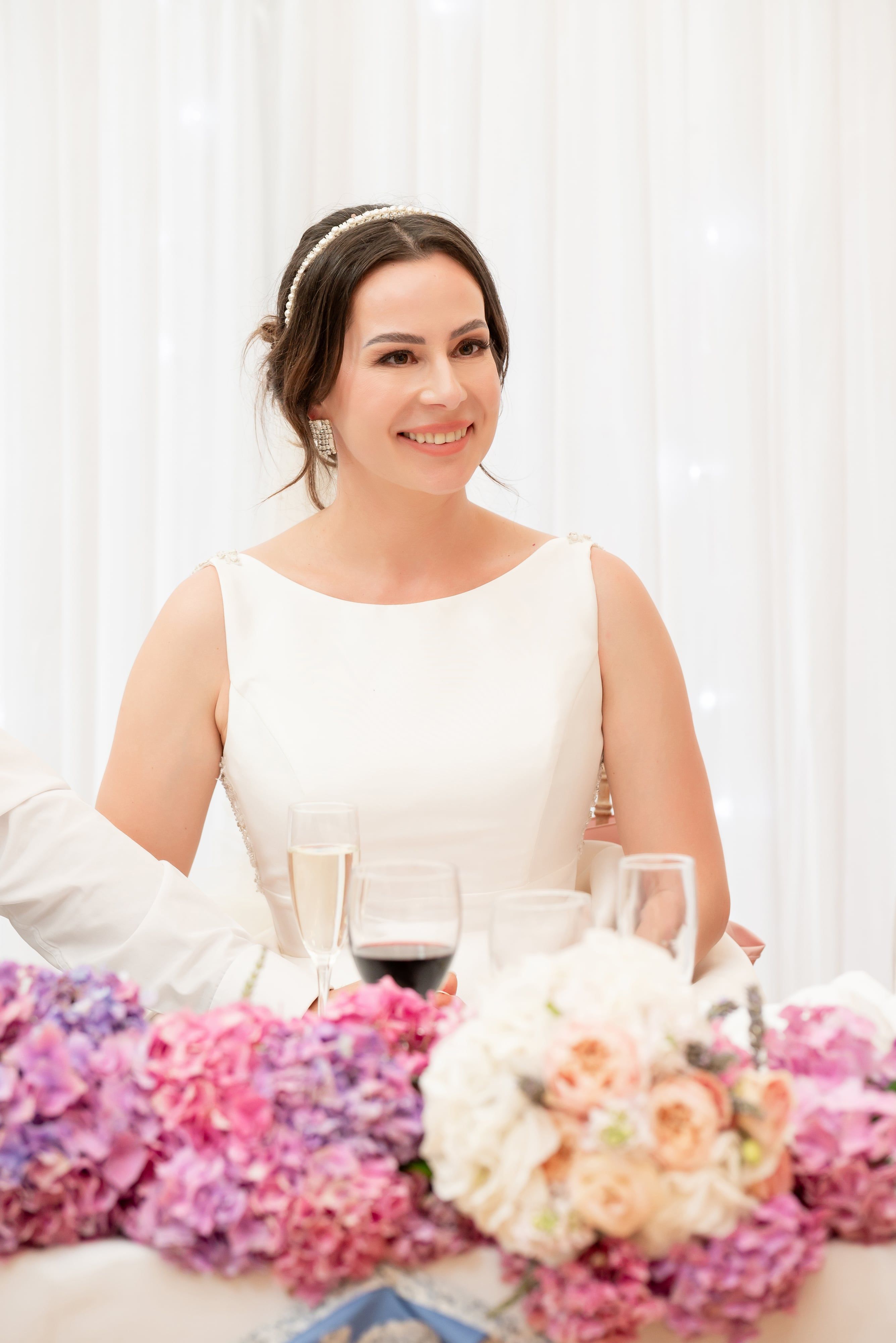 Bride smiles at the top table behind pink and purple hydrangeas