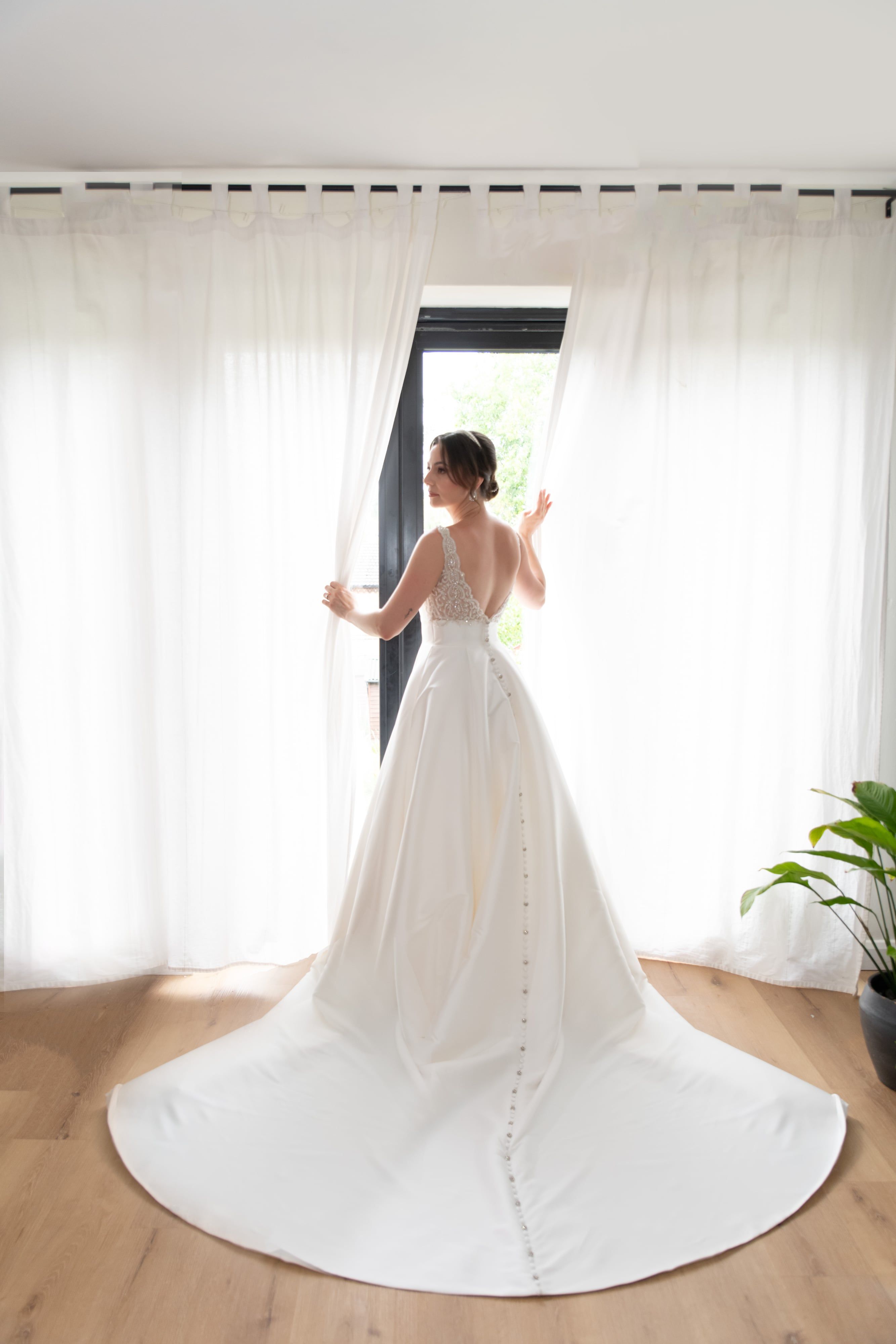Bride photographed from behind at the window, button-back train sweeping the floor