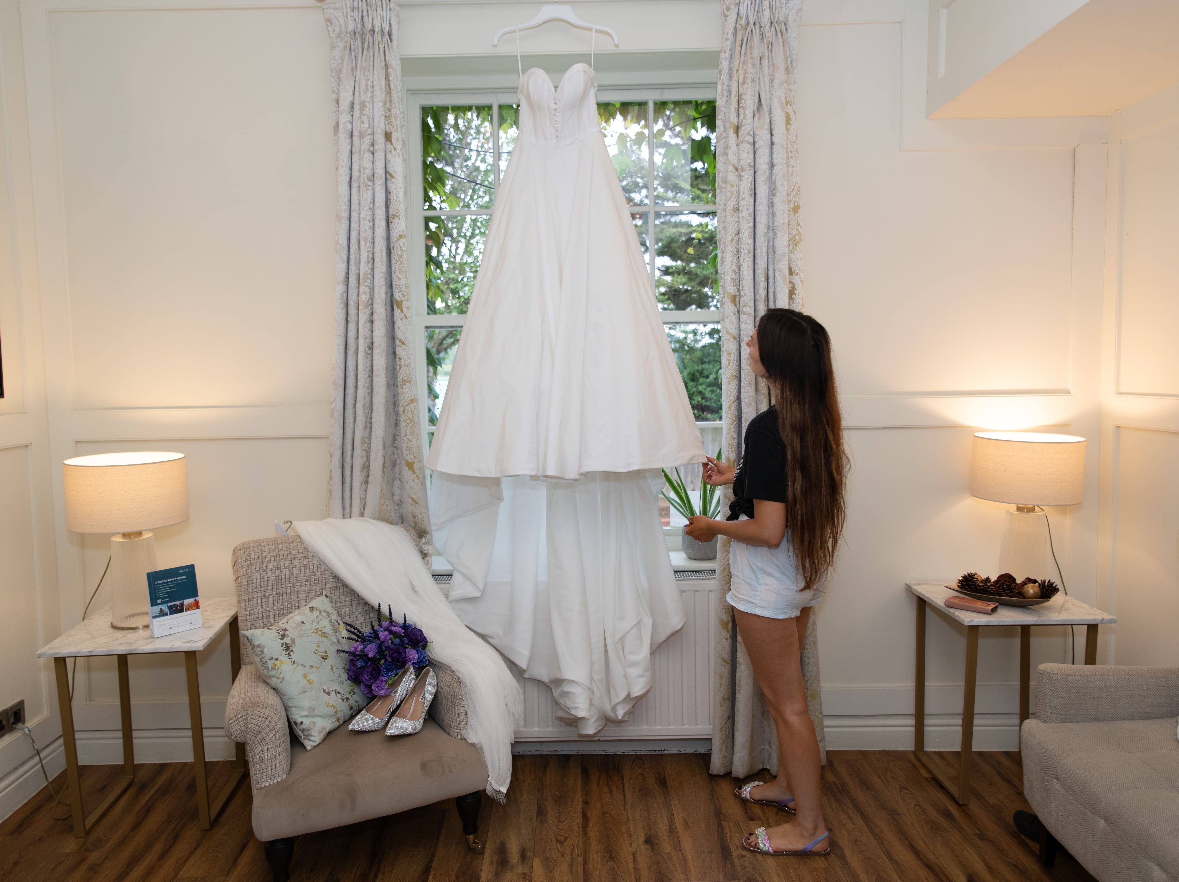 Wedding dress hangs in the tall window of the Holiday Inn Milton Keynes East room during bridal preparations