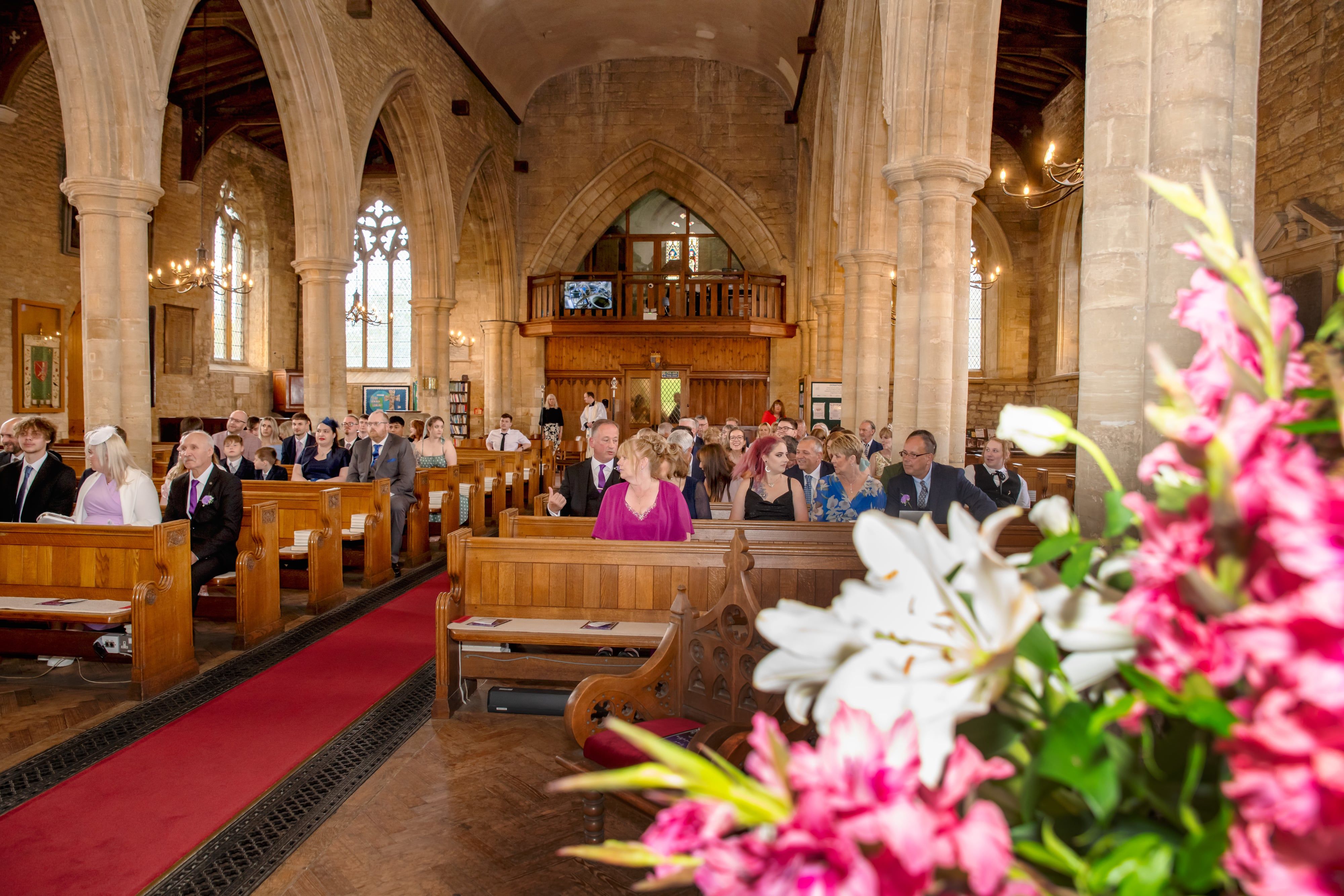 Guests fill the mediaeval nave of Olney parish church before the ceremony, lilies in the foreground