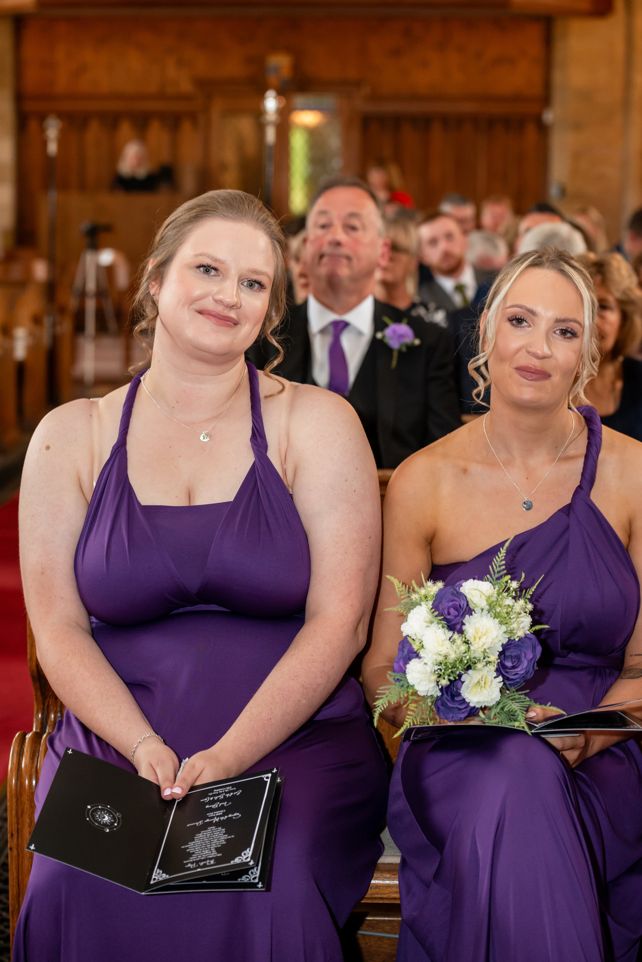 Bridesmaids in purple gowns seated in the pews with white and purple bouquets